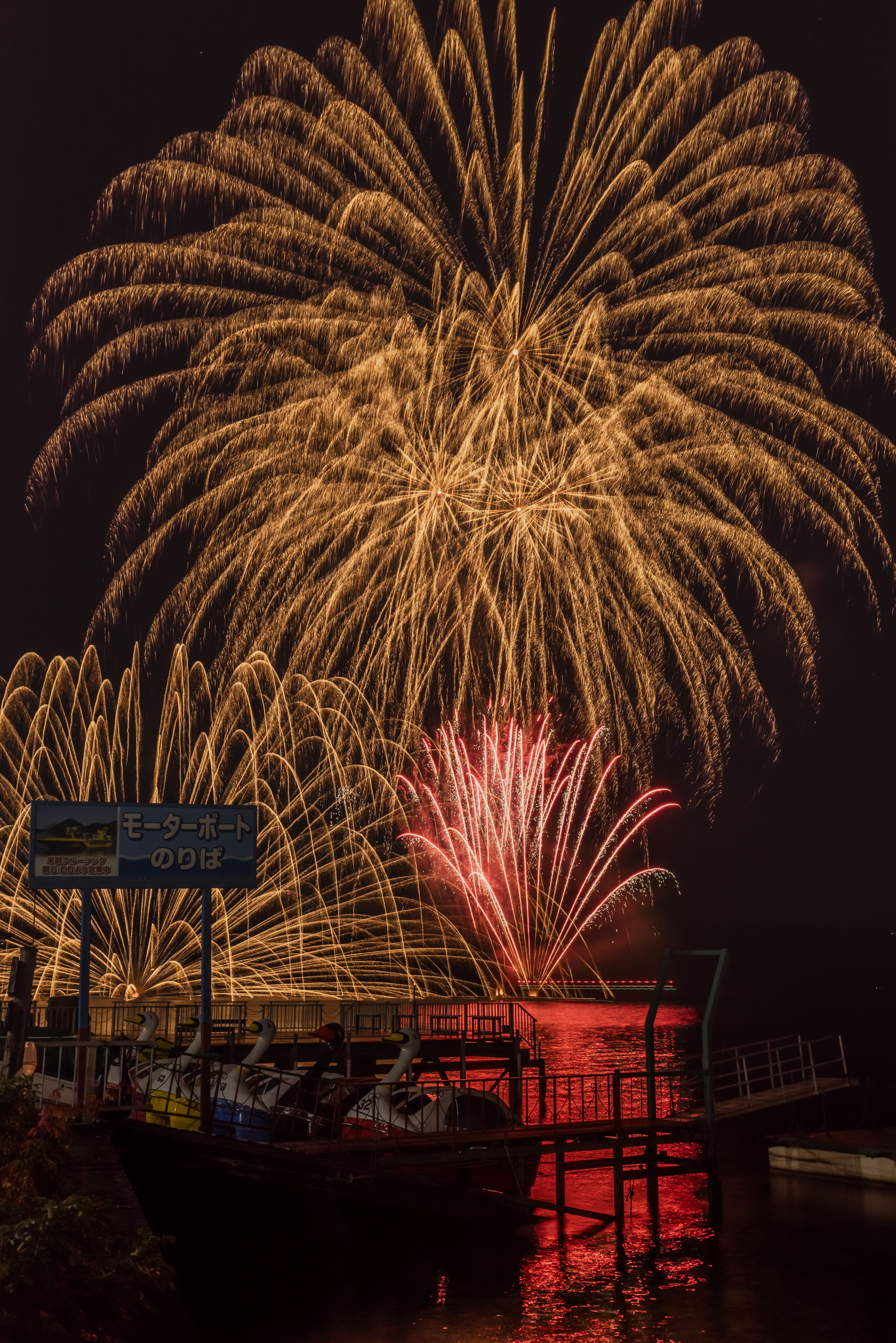 A beautiful scene of golden and red fireworks illuminating the night sky and reflecting on the water