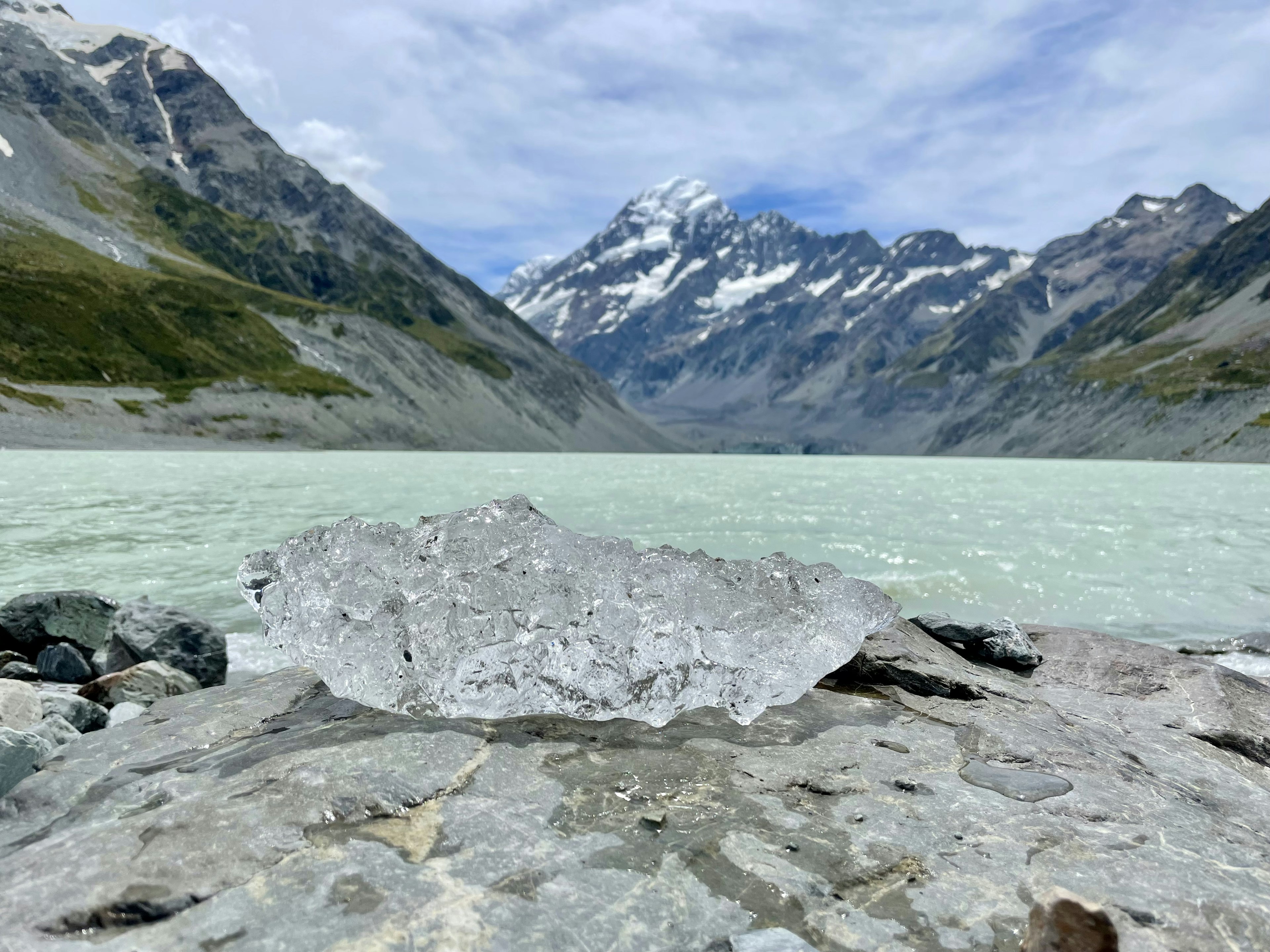 Transparent ice block on rocky glacier landscape with snow-capped mountains