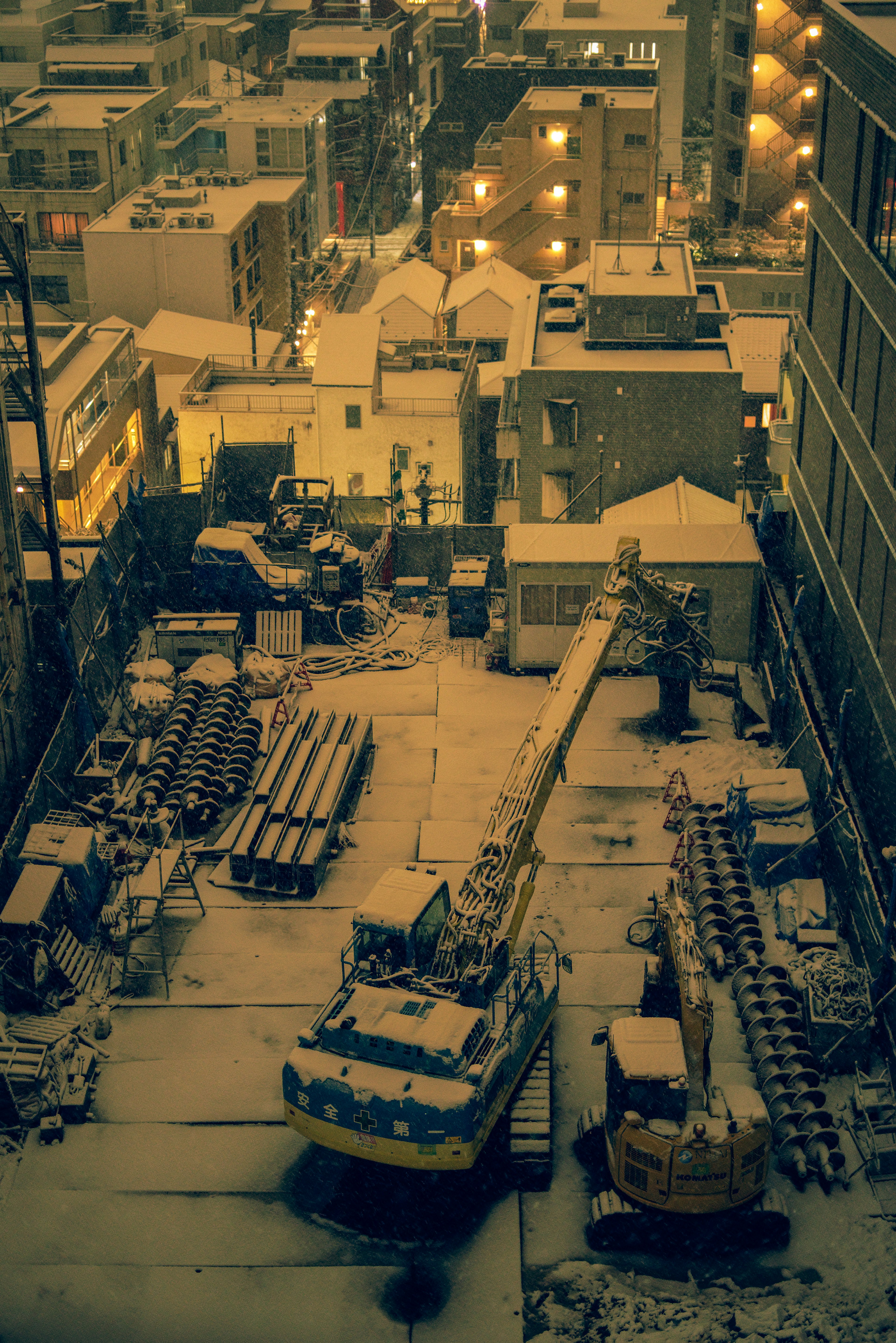 Vista nocturna de un sitio de construcción nevado con grúas y materiales de construcción