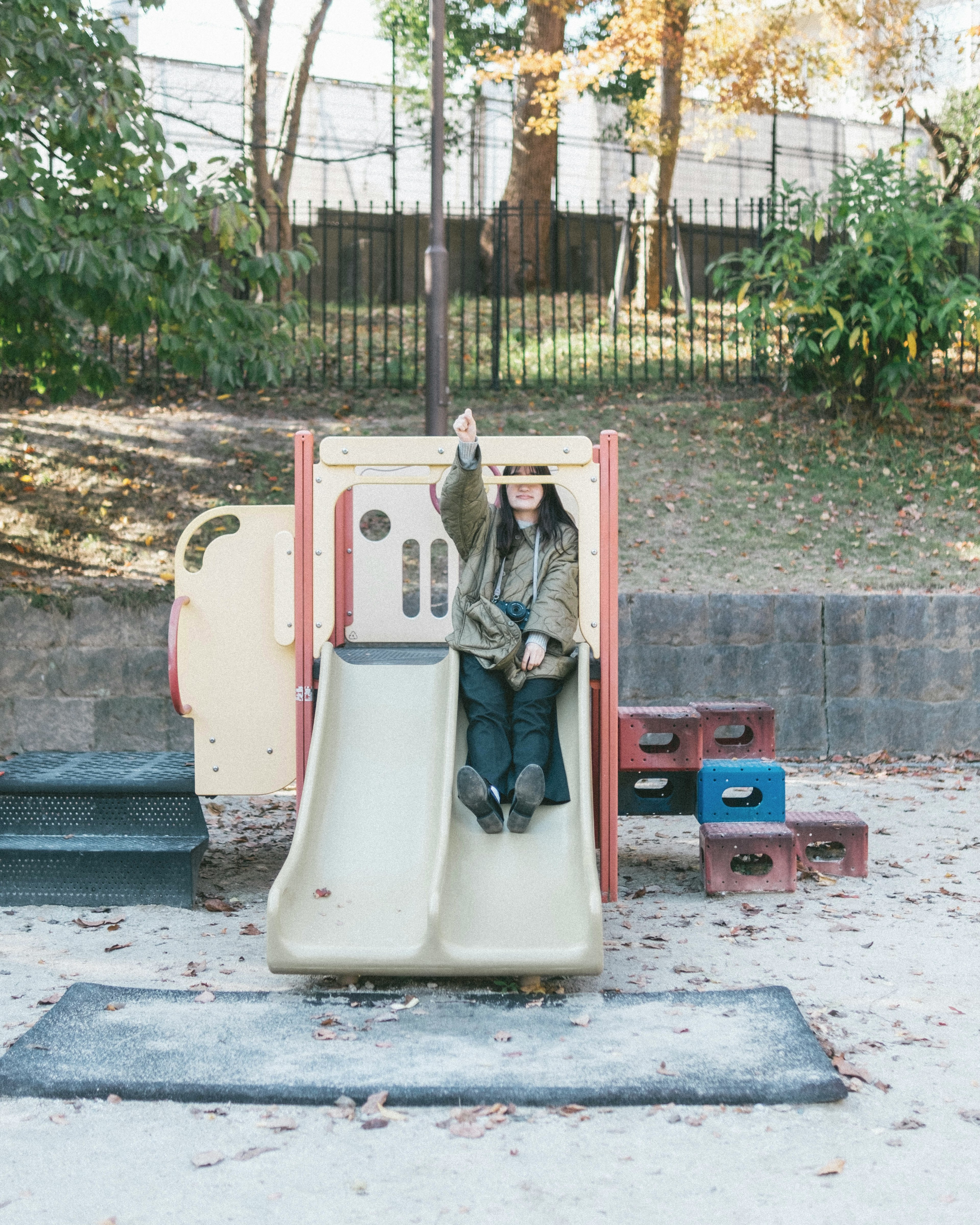 Child sitting on a playground slide with hand raised