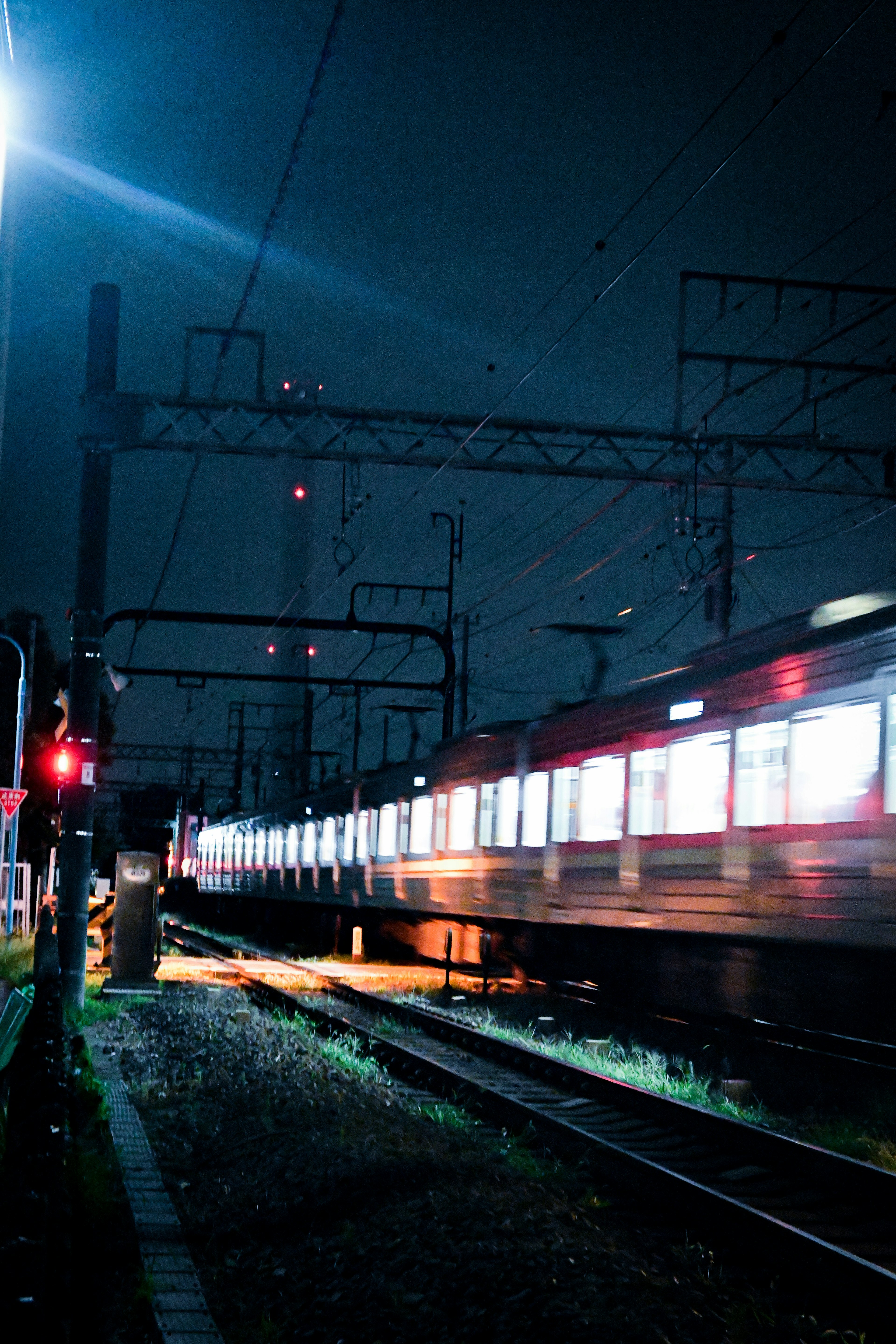 Kereta yang bergerak di malam hari dengan sinyal dan rel yang diterangi