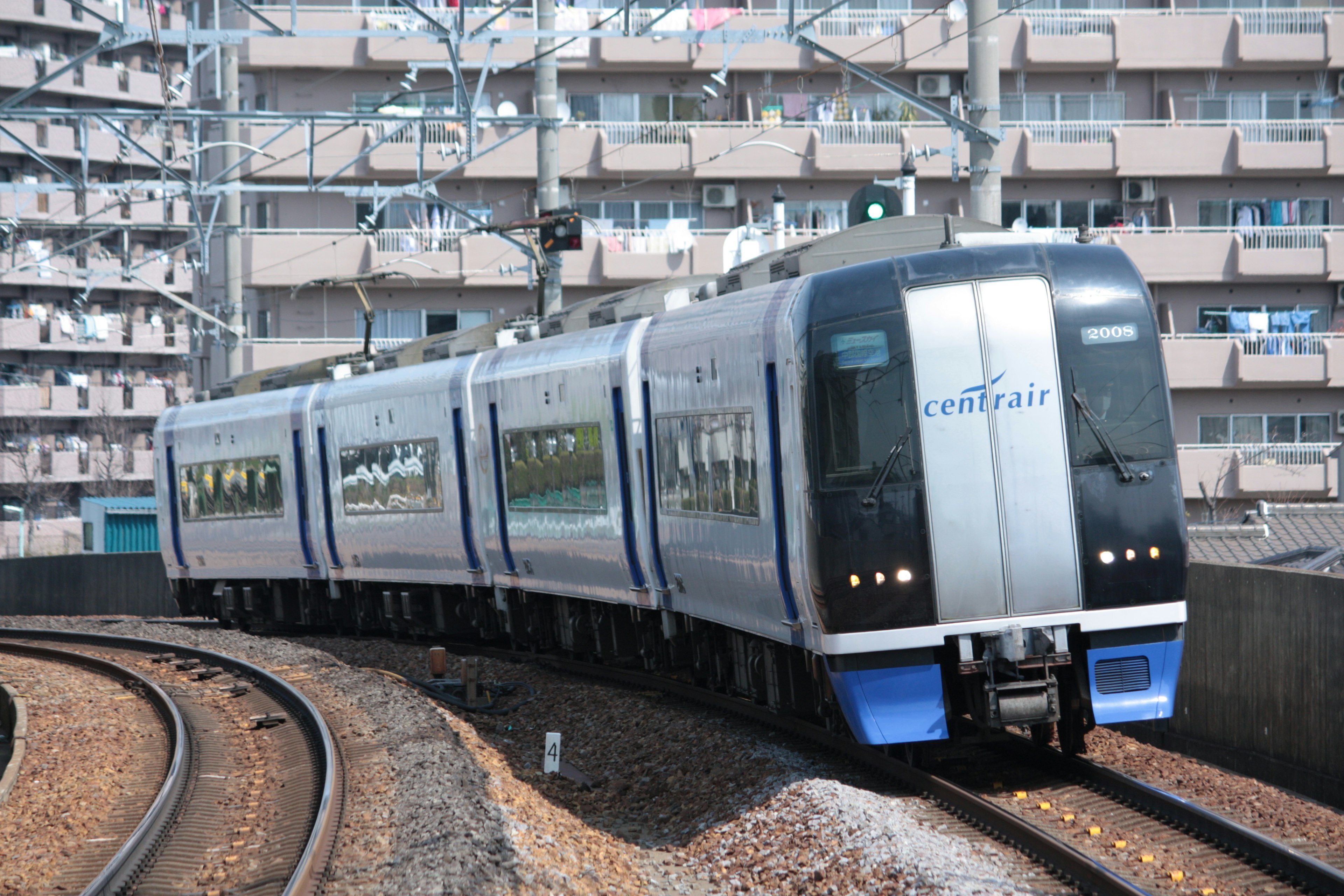 曲がり角を回る青と銀の電車と高層ビル群