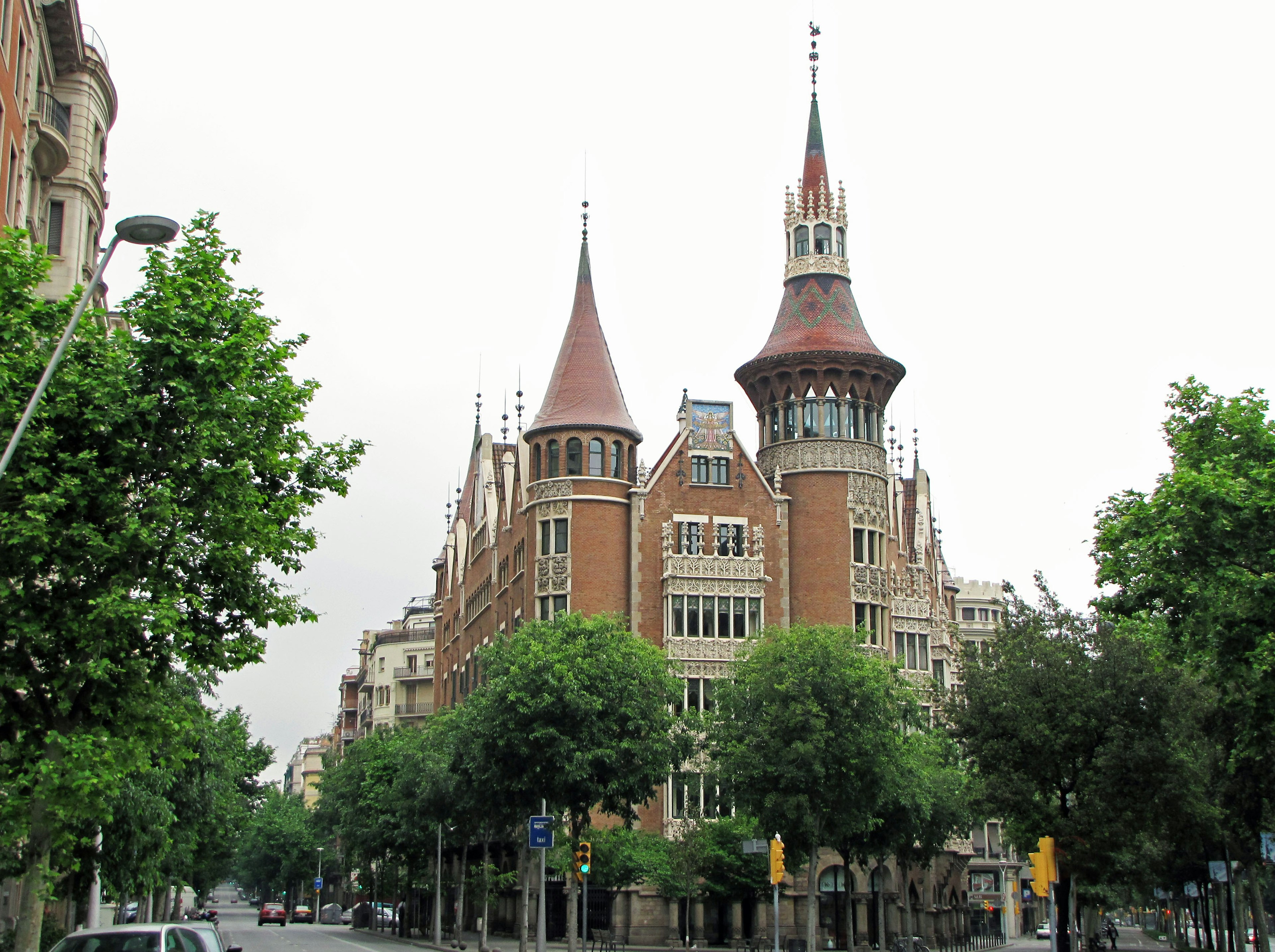 Historisches Gebäude aus rotem Ziegel mit spitzen Türmen umgeben von grünen Bäumen