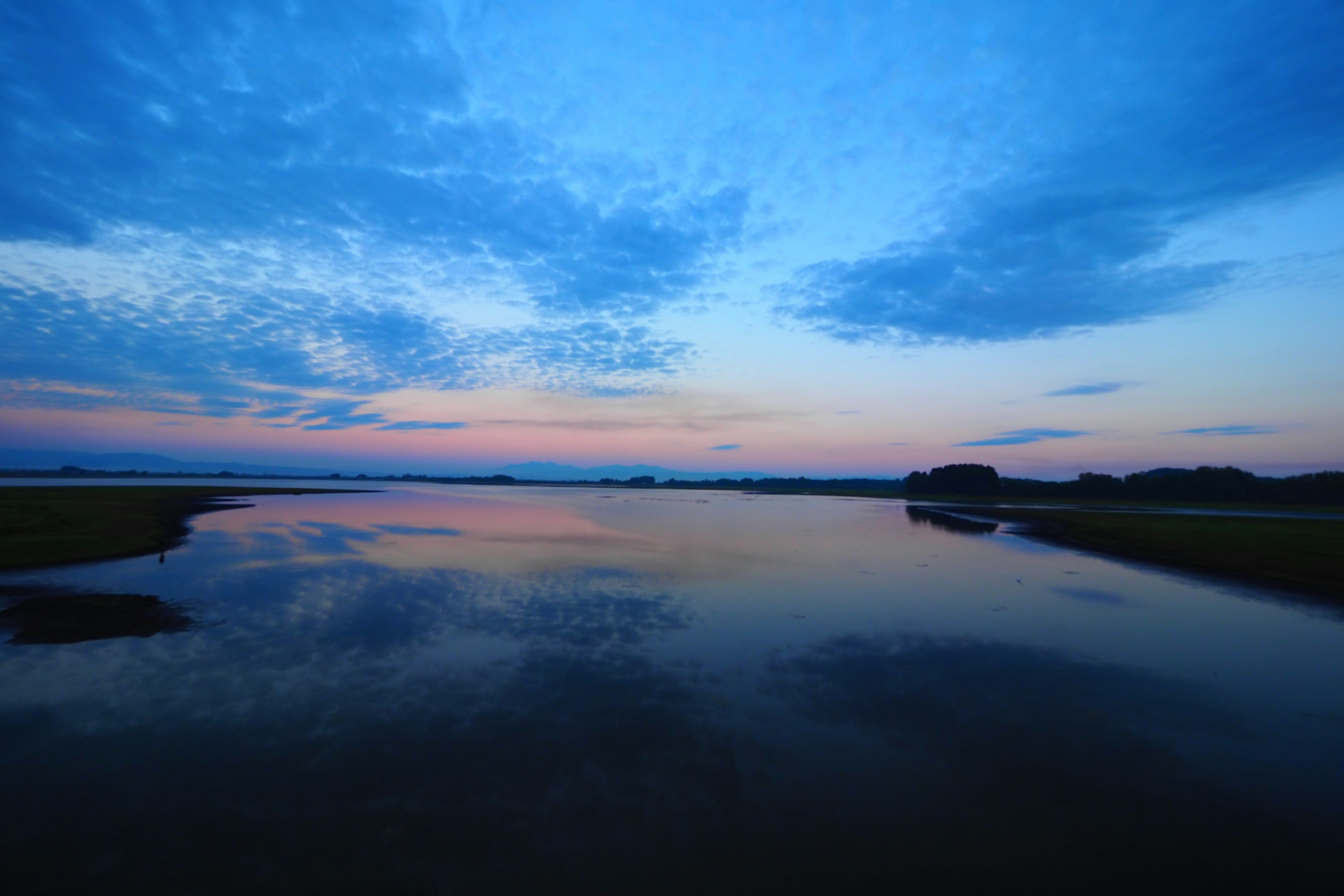 静かな水面に映る青い空と夕焼けの色合いが美しい風景