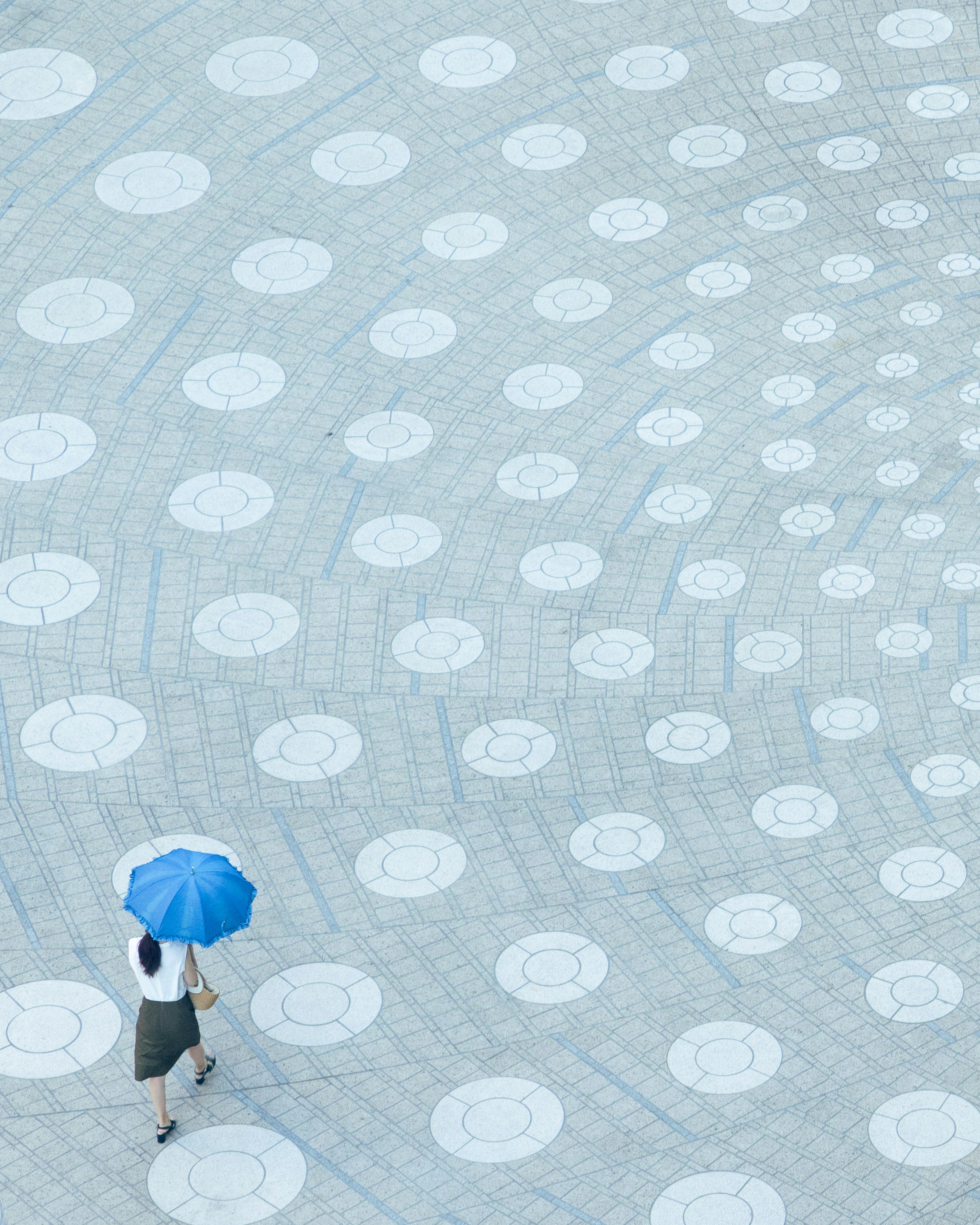 A woman with a blue umbrella walking on a patterned floor with circular designs