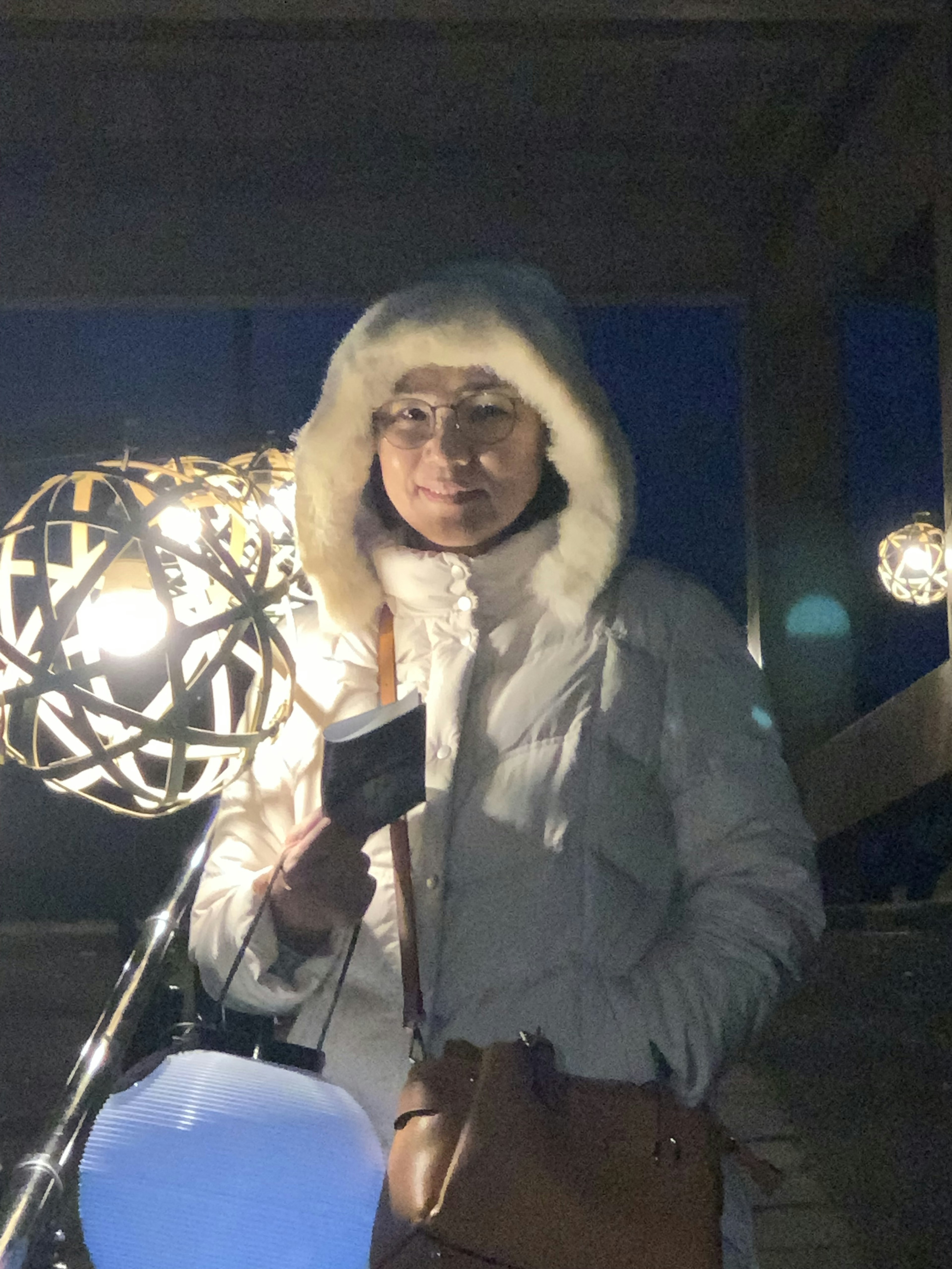 Une femme debout dans une doudoune blanche la nuit Des lumières décoratives brillent en arrière-plan