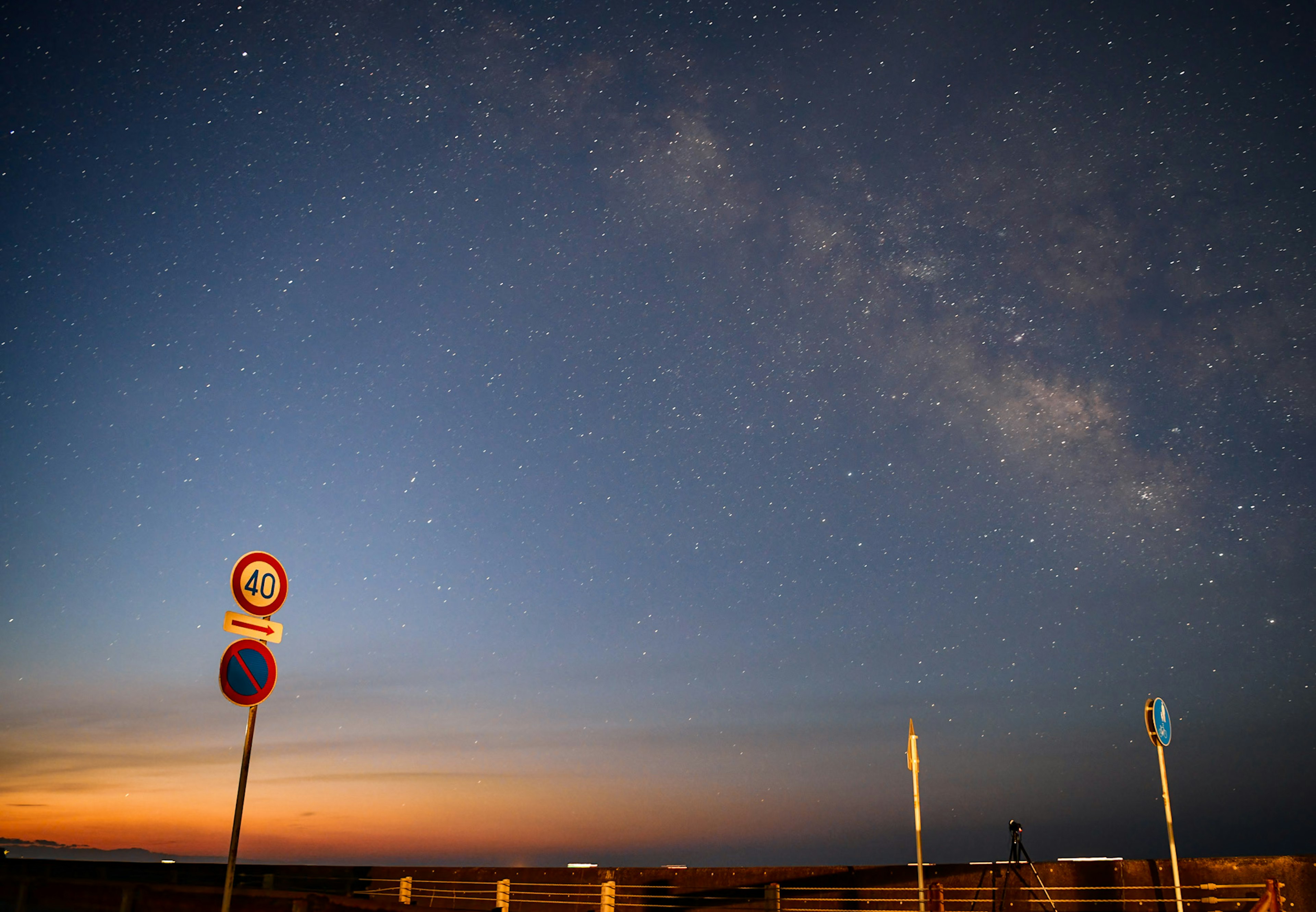 星空と夕焼けの海岸風景に交通標識が立つ