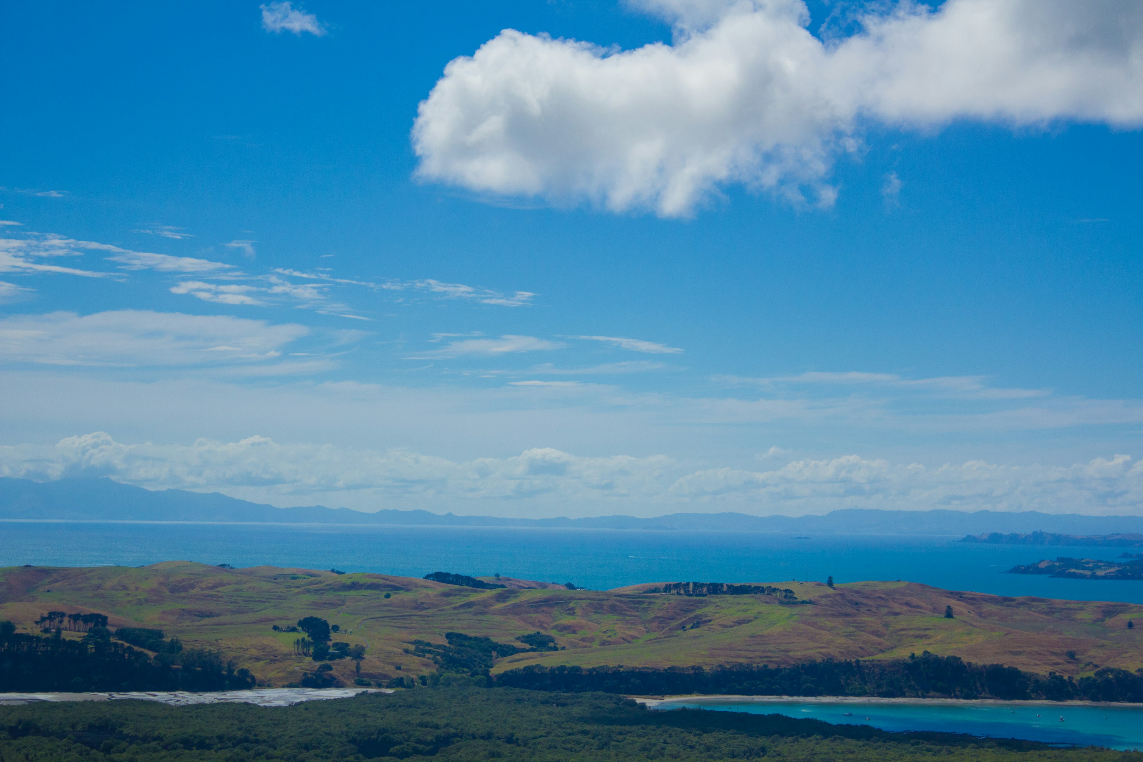 Landschaft mit blauem Himmel weißen Wolken grünen Hügeln und blauem Ozean