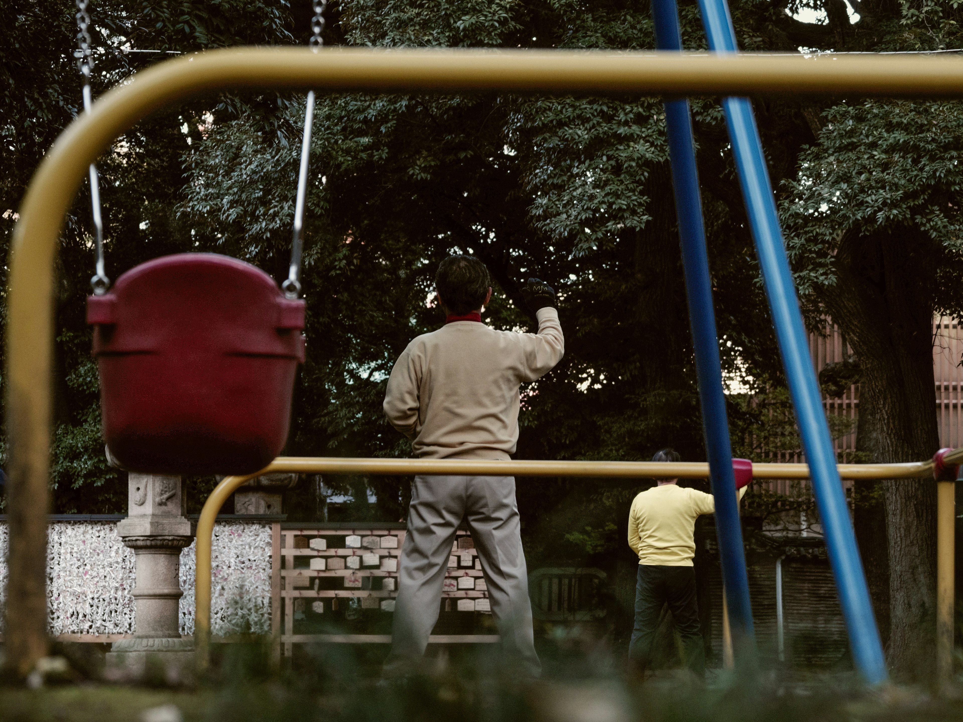 Child and adult playing in a park visible from behind colorful playground equipment