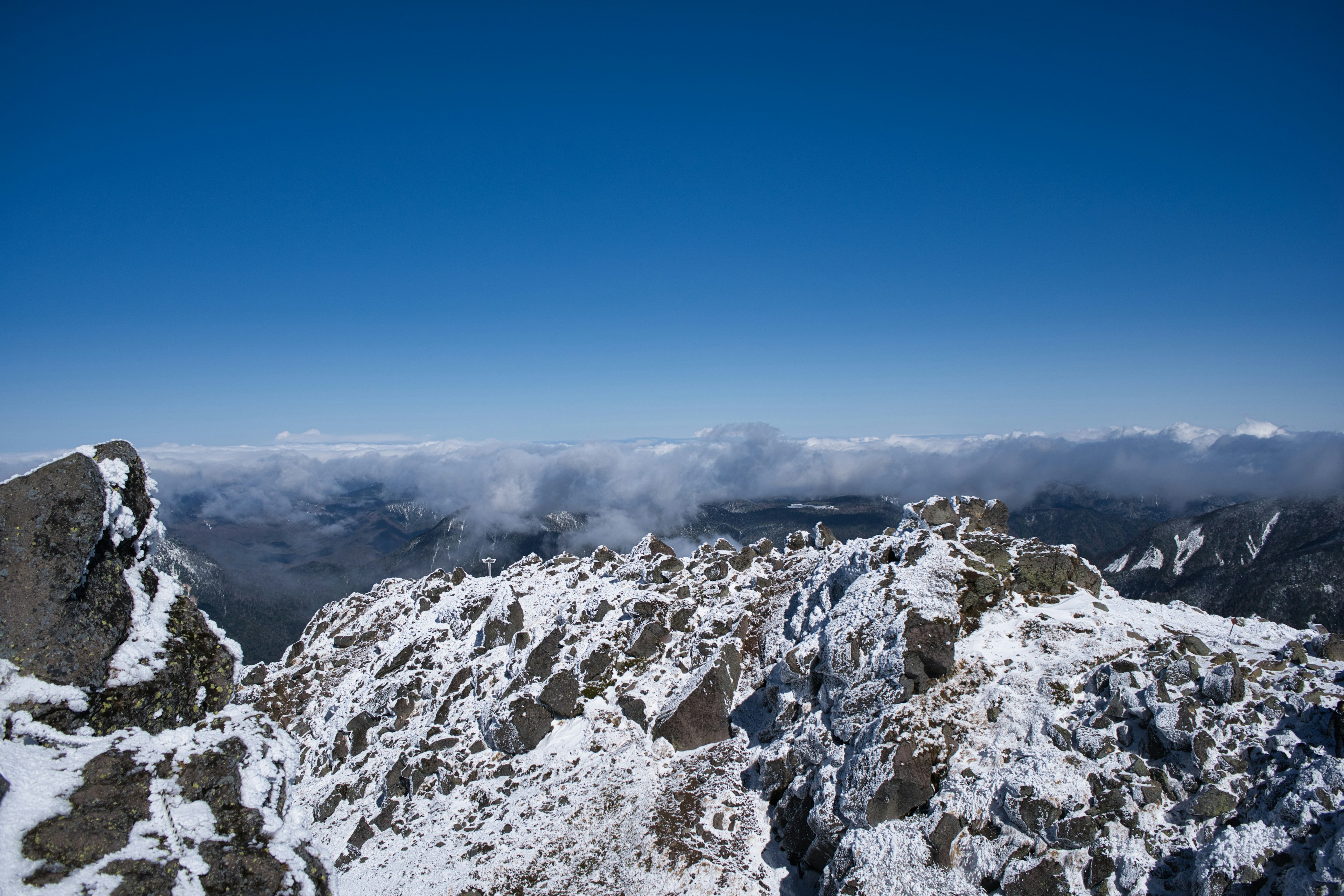 Aussicht von einem schneebedeckten Berggipfel mit klarem blauen Himmel und fernen Wolken