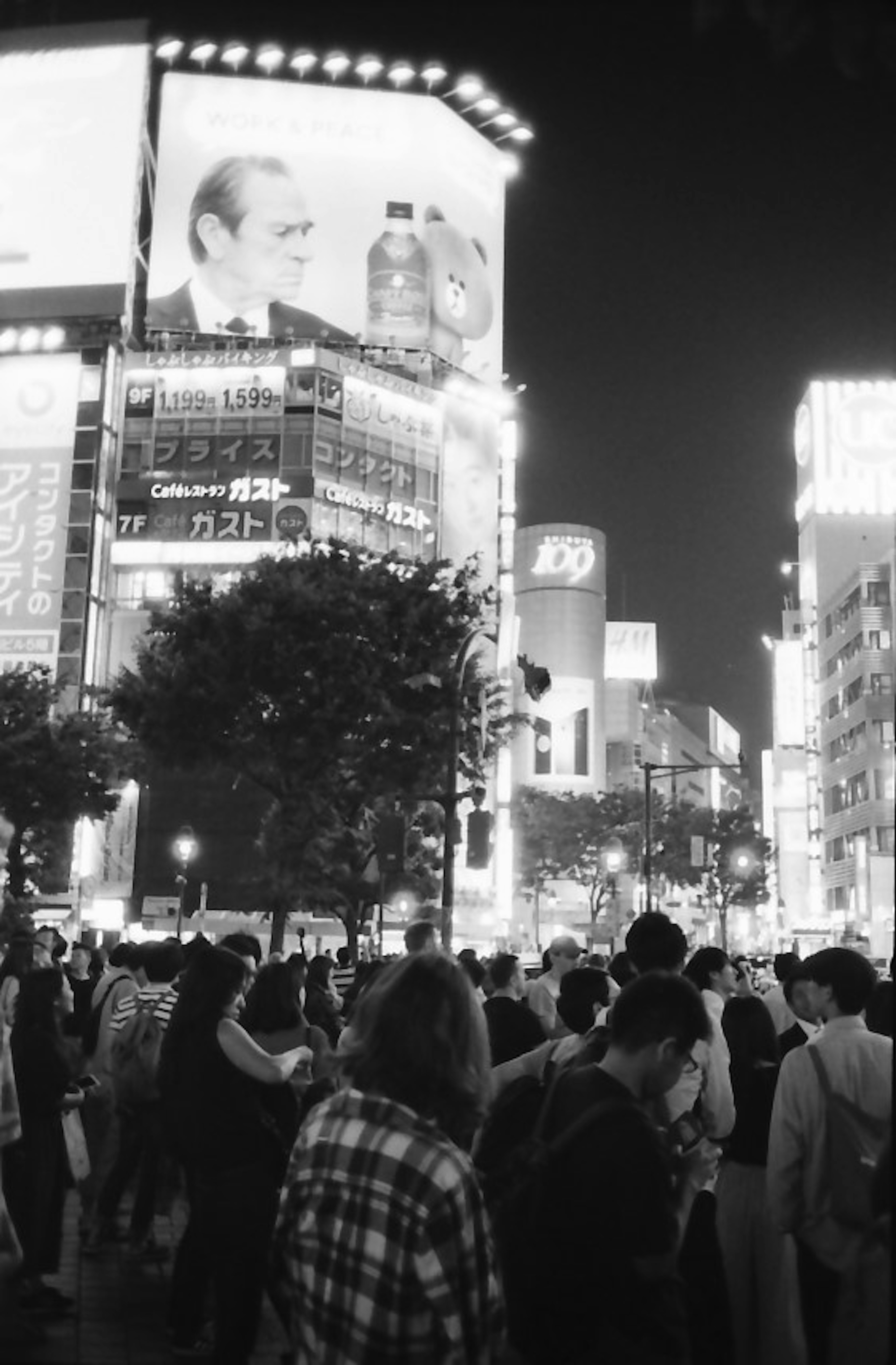 Kerumunan berkumpul di Shibuya di malam hari dengan gedung dan iklan yang cerah