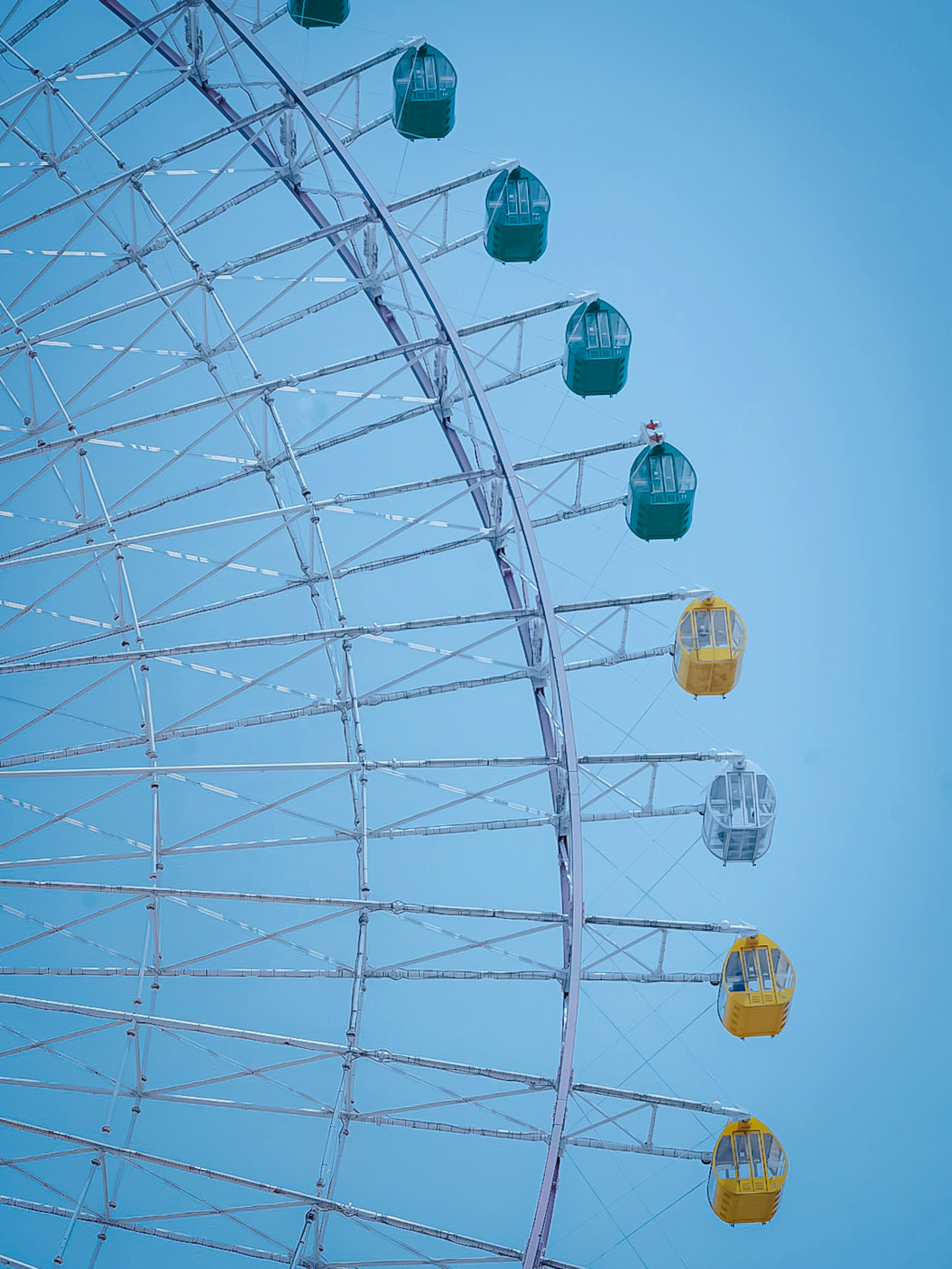 Part of a large Ferris wheel with colorful capsules against a blue sky