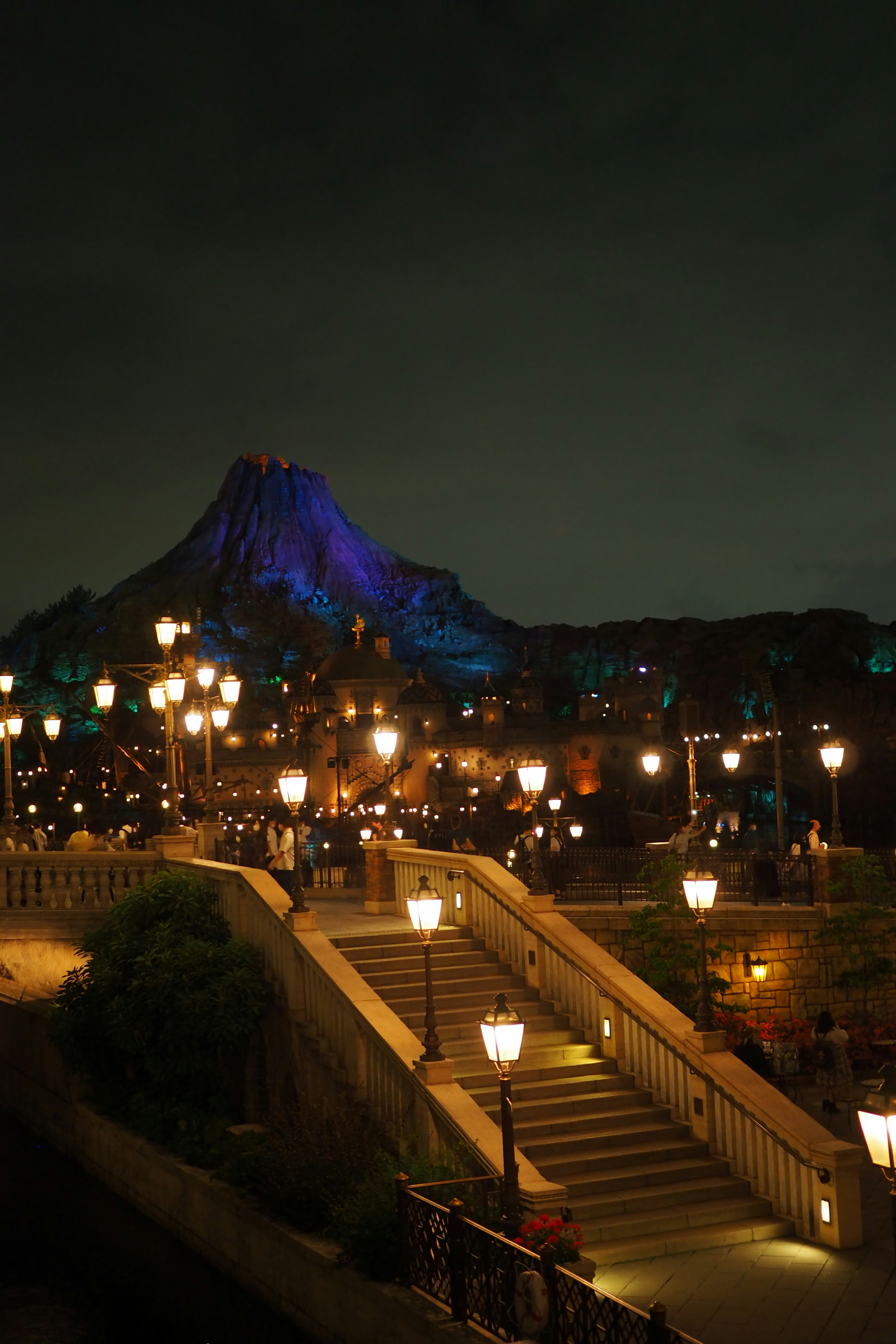 A beautiful night scene featuring illuminated stairs and street lamps with a glowing mountain in the background