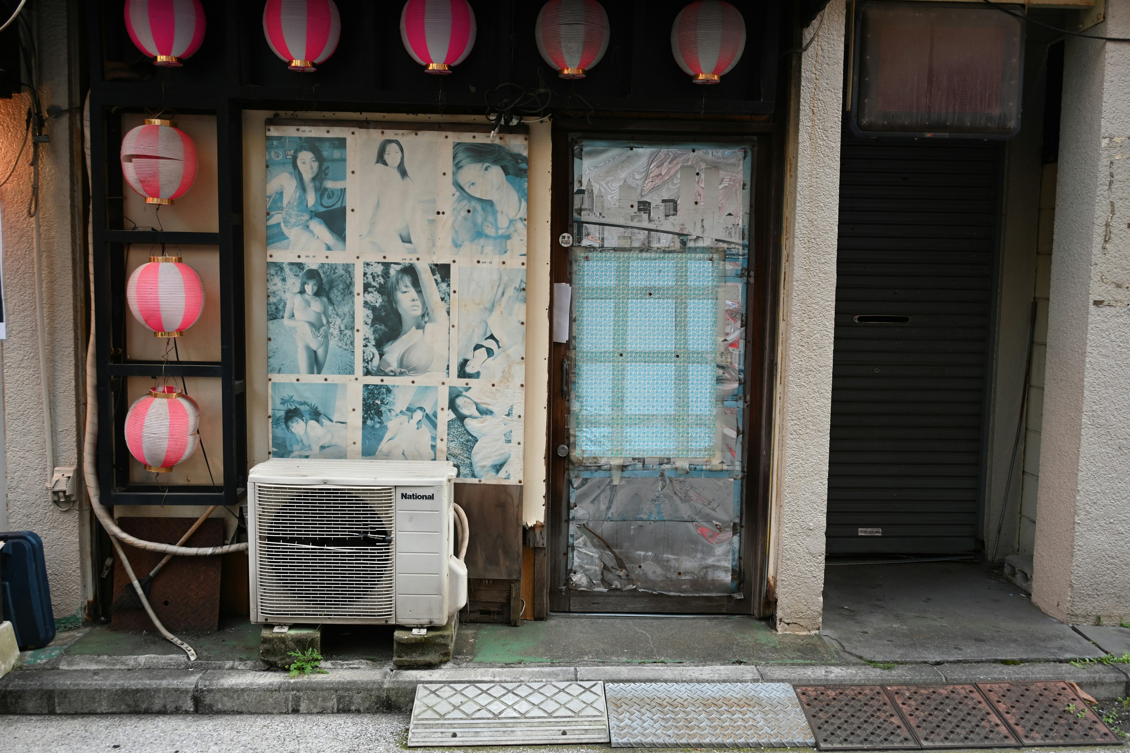 Old wooden building wall with pasted photos and dark door next to red lanterns