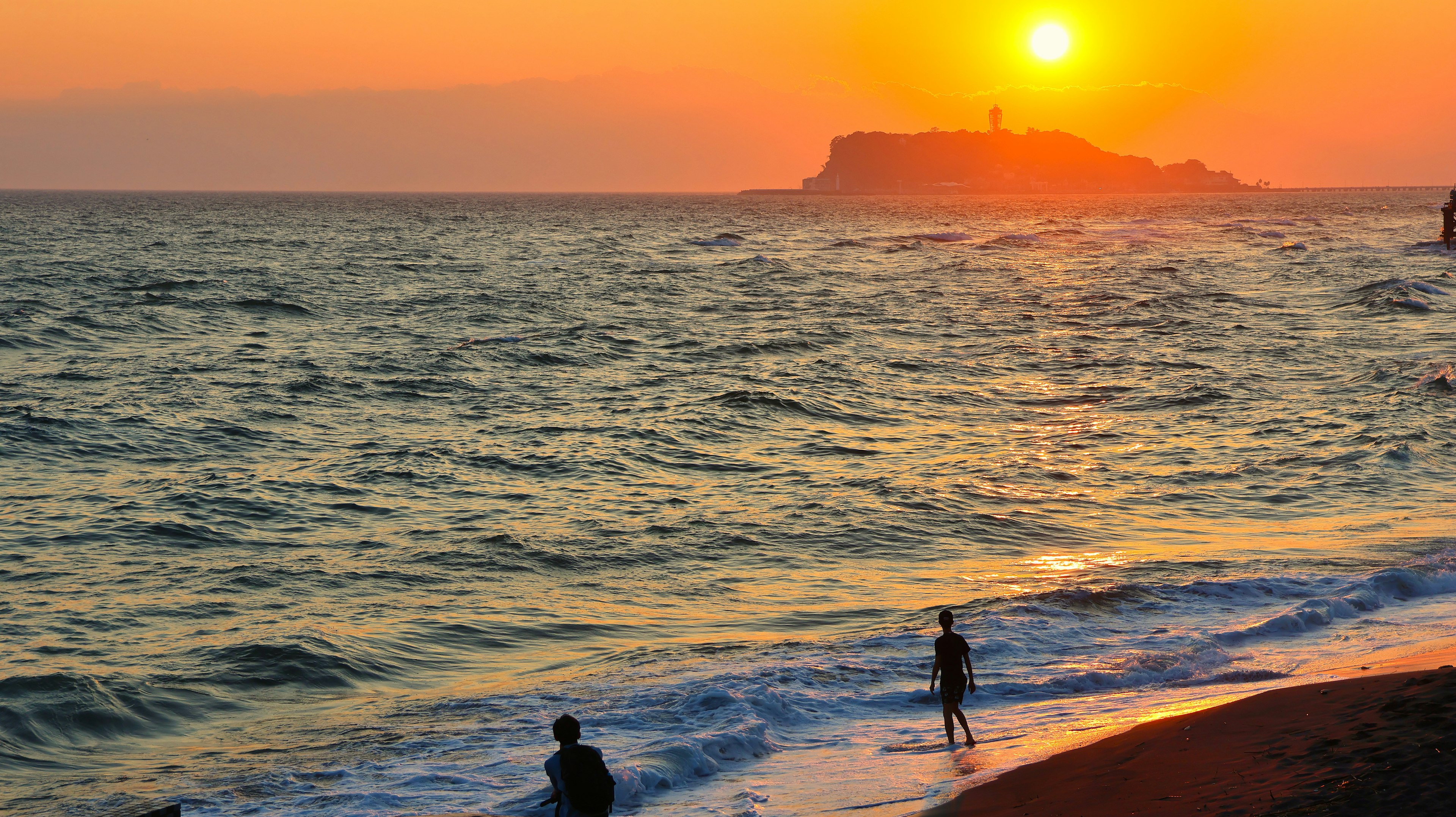 夕日が海に沈む美しい風景と人々が遊ぶ浜辺