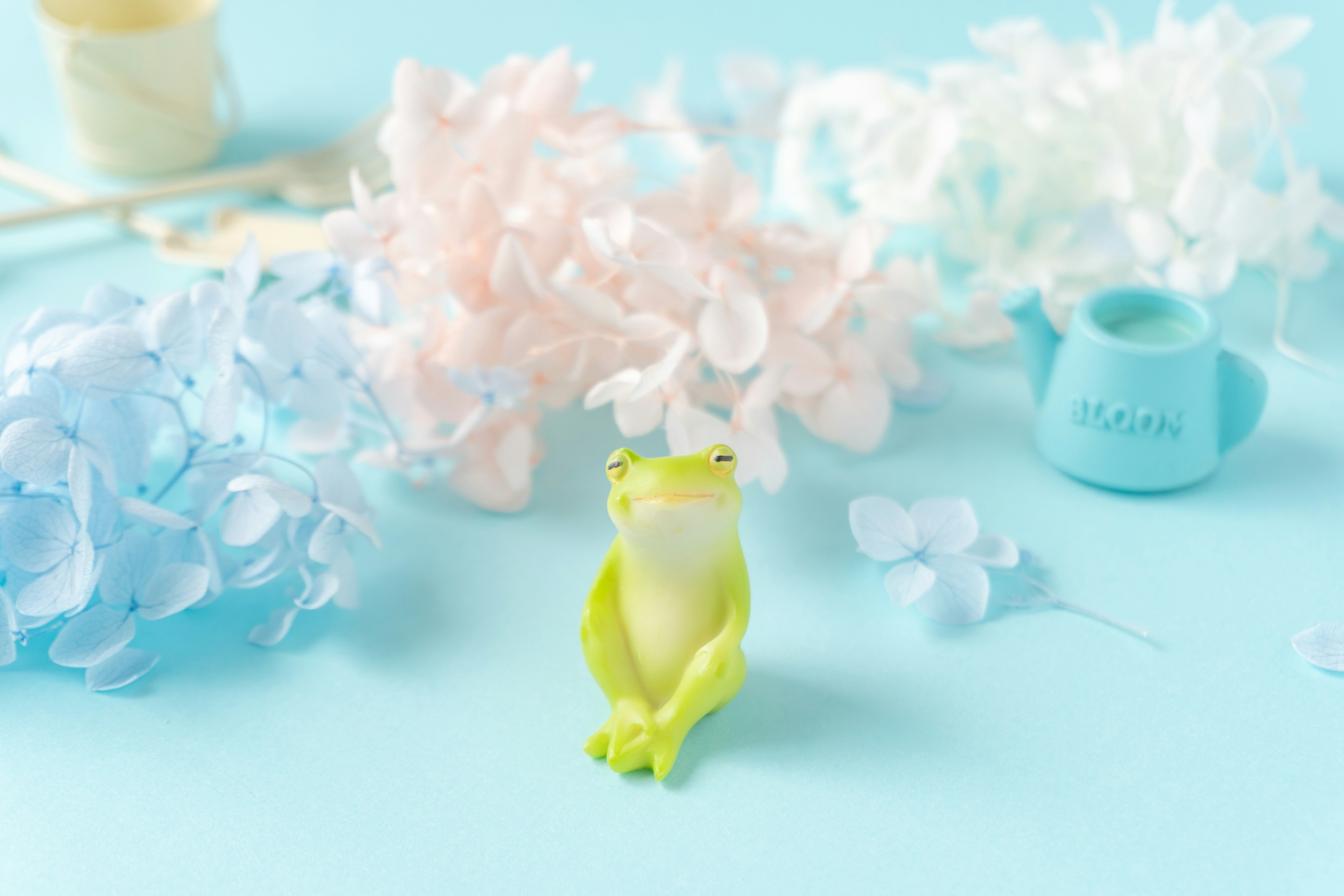 A green frog sitting on a blue background surrounded by pastel-colored flowers