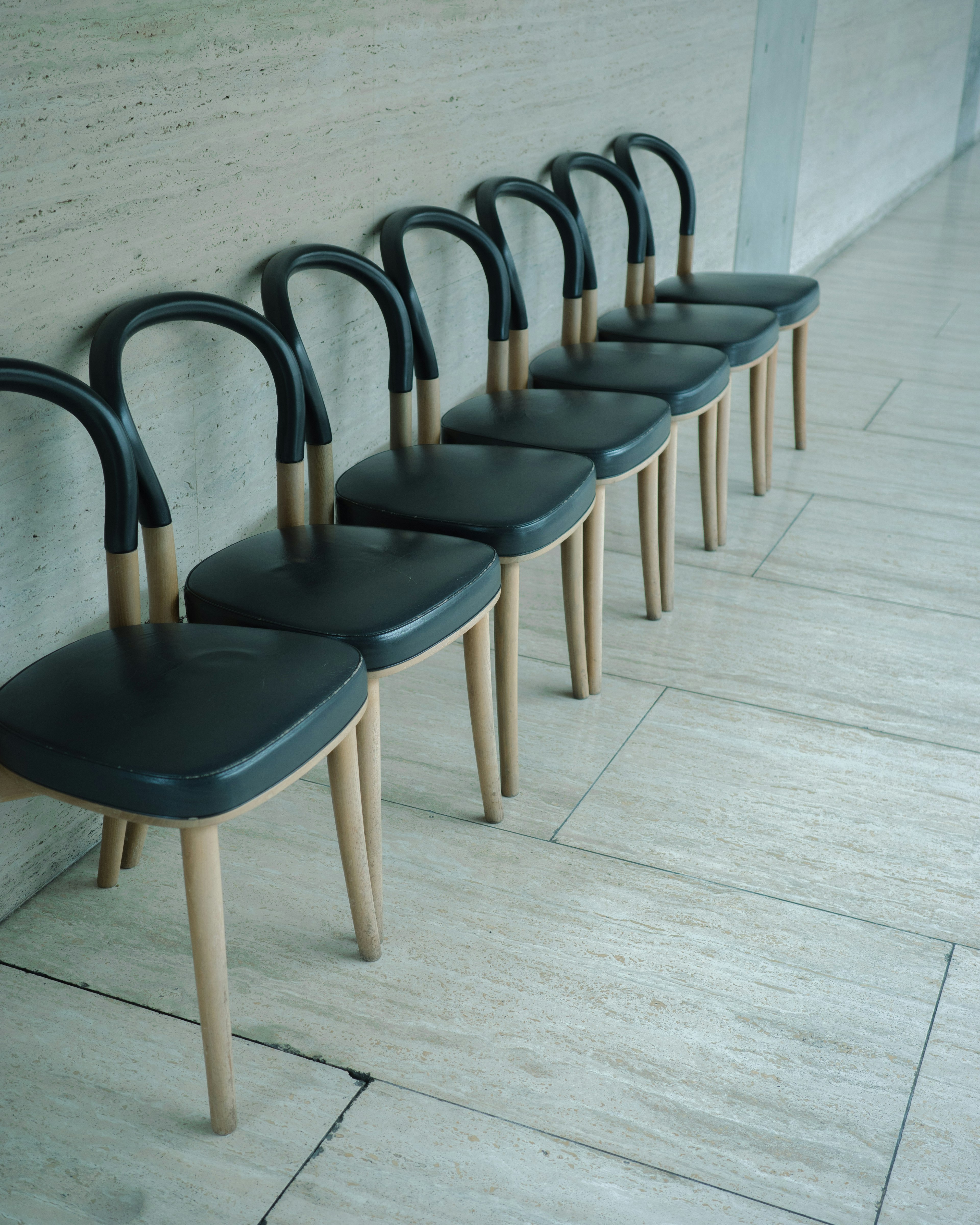 Une rangée de chaises avec des pieds en bois et des sièges noirs disposées de manière ordonnée