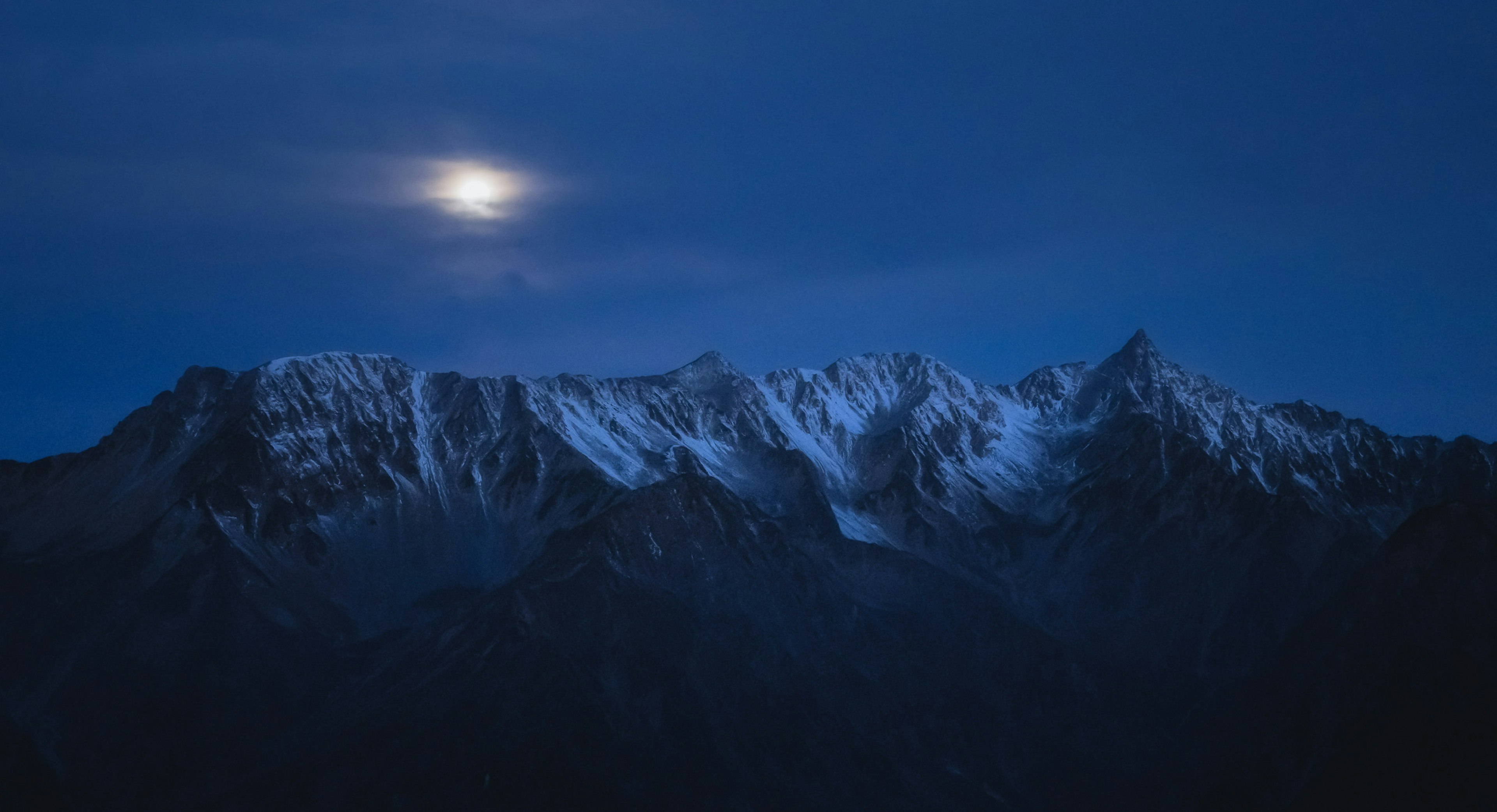 Montañas cubiertas de nieve bajo un cielo nocturno azul con una luna brillante