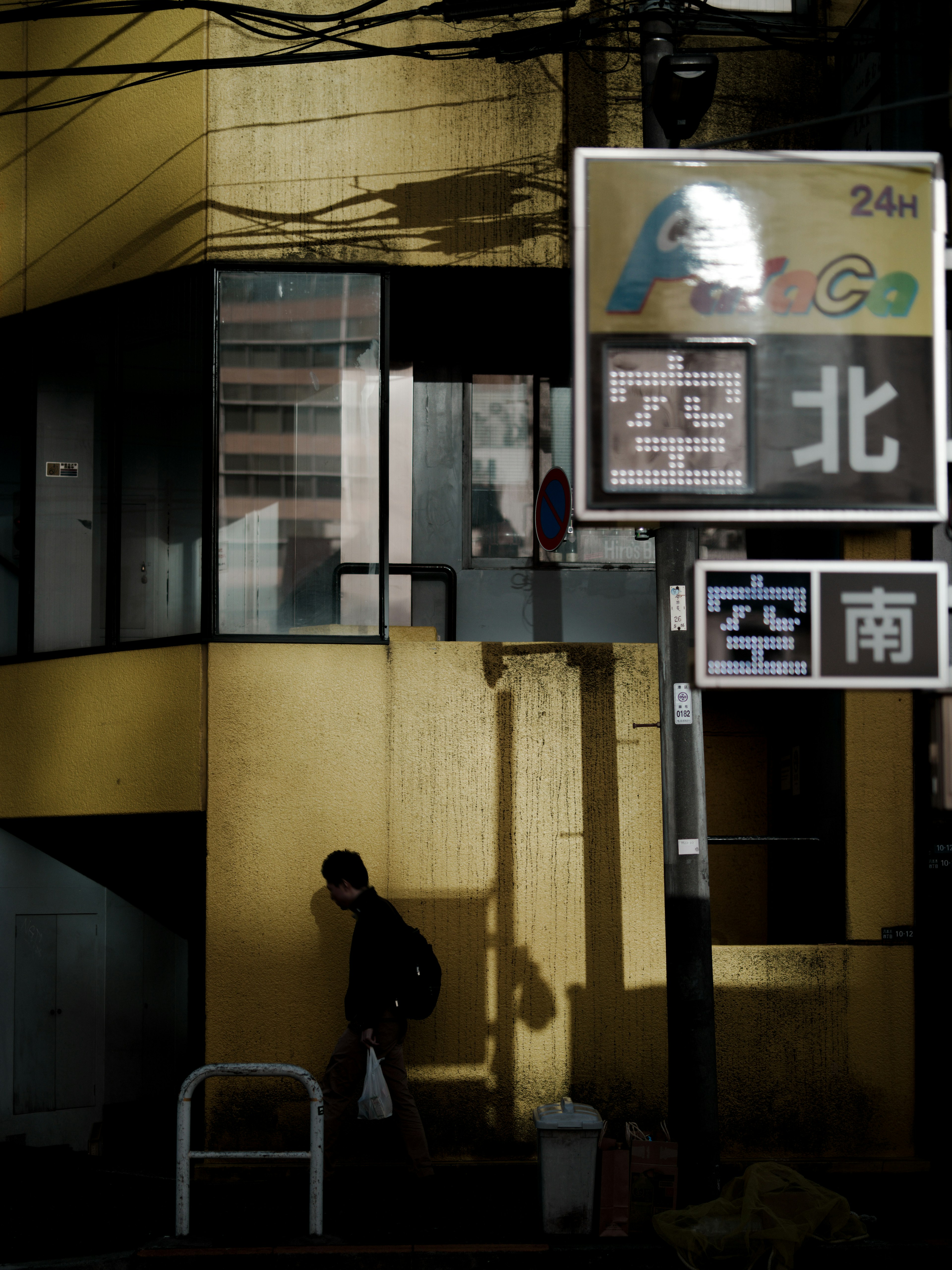 Shadowy urban scene featuring a yellow building and signs with a person walking