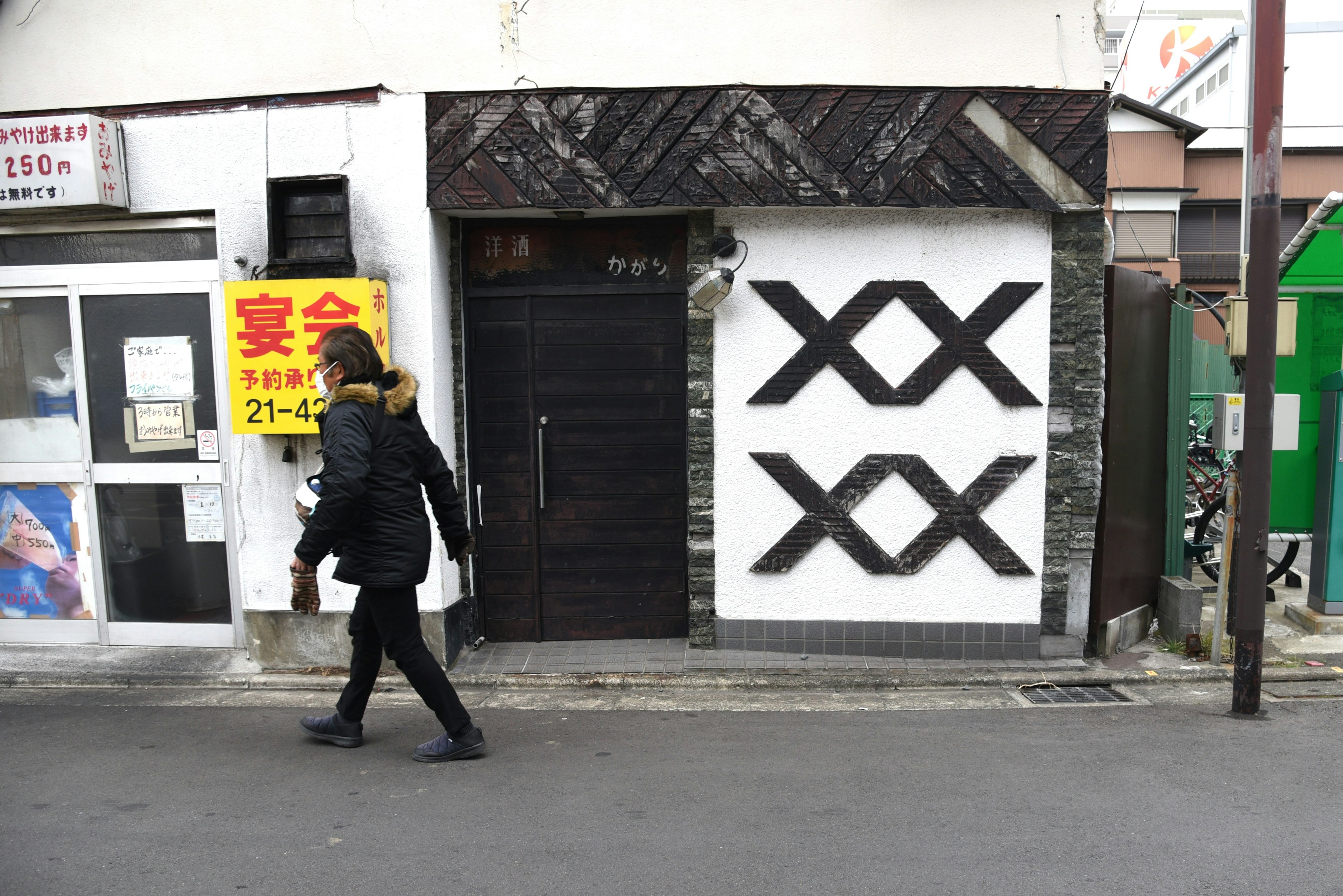 A person walking in front of a building with a white wall featuring black patterns