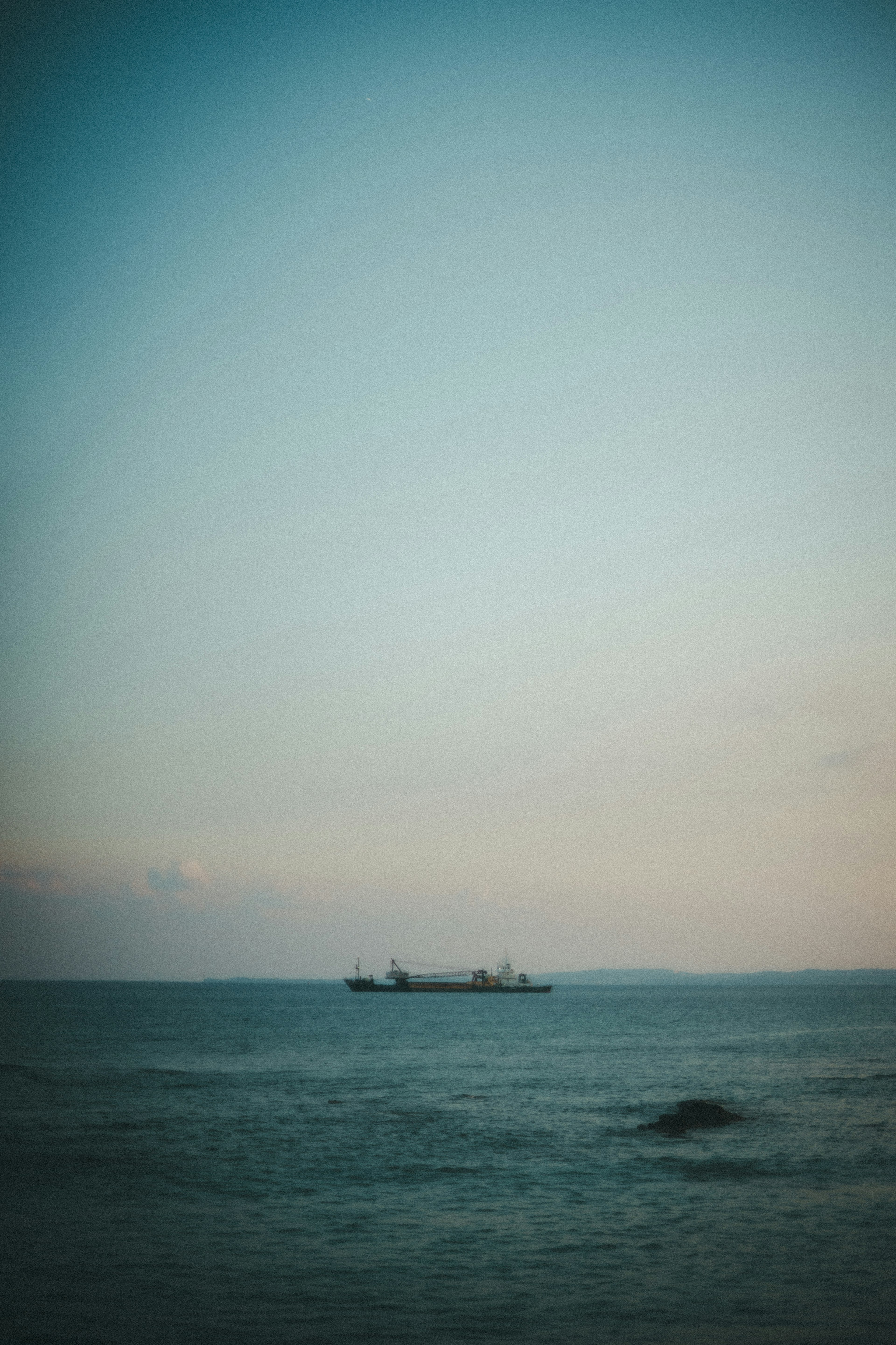 A ship floating on a blue ocean with a soft sky background