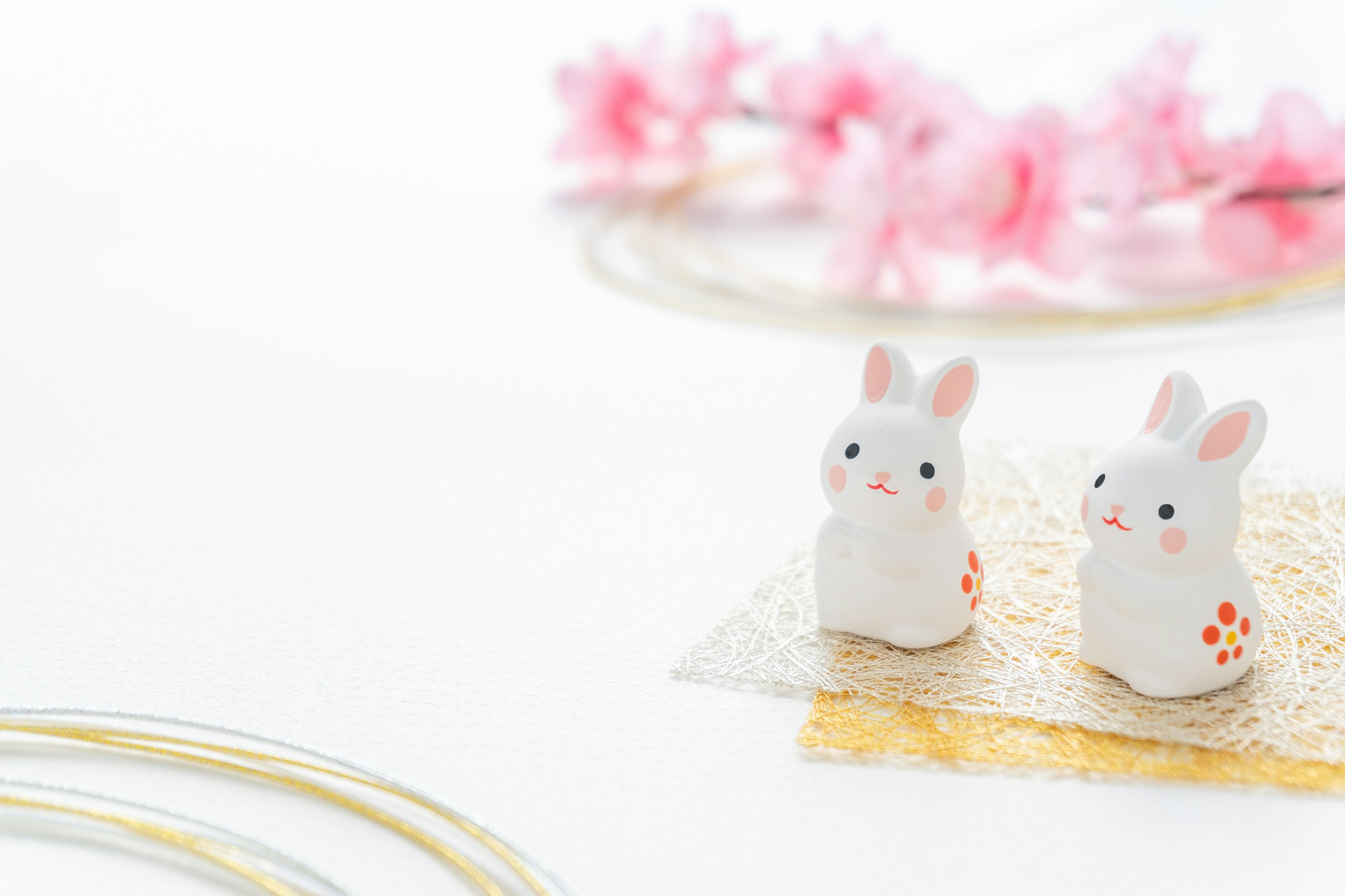 Deux figurines de lapins blancs avec des détails floraux entourées de cerisiers en fleurs