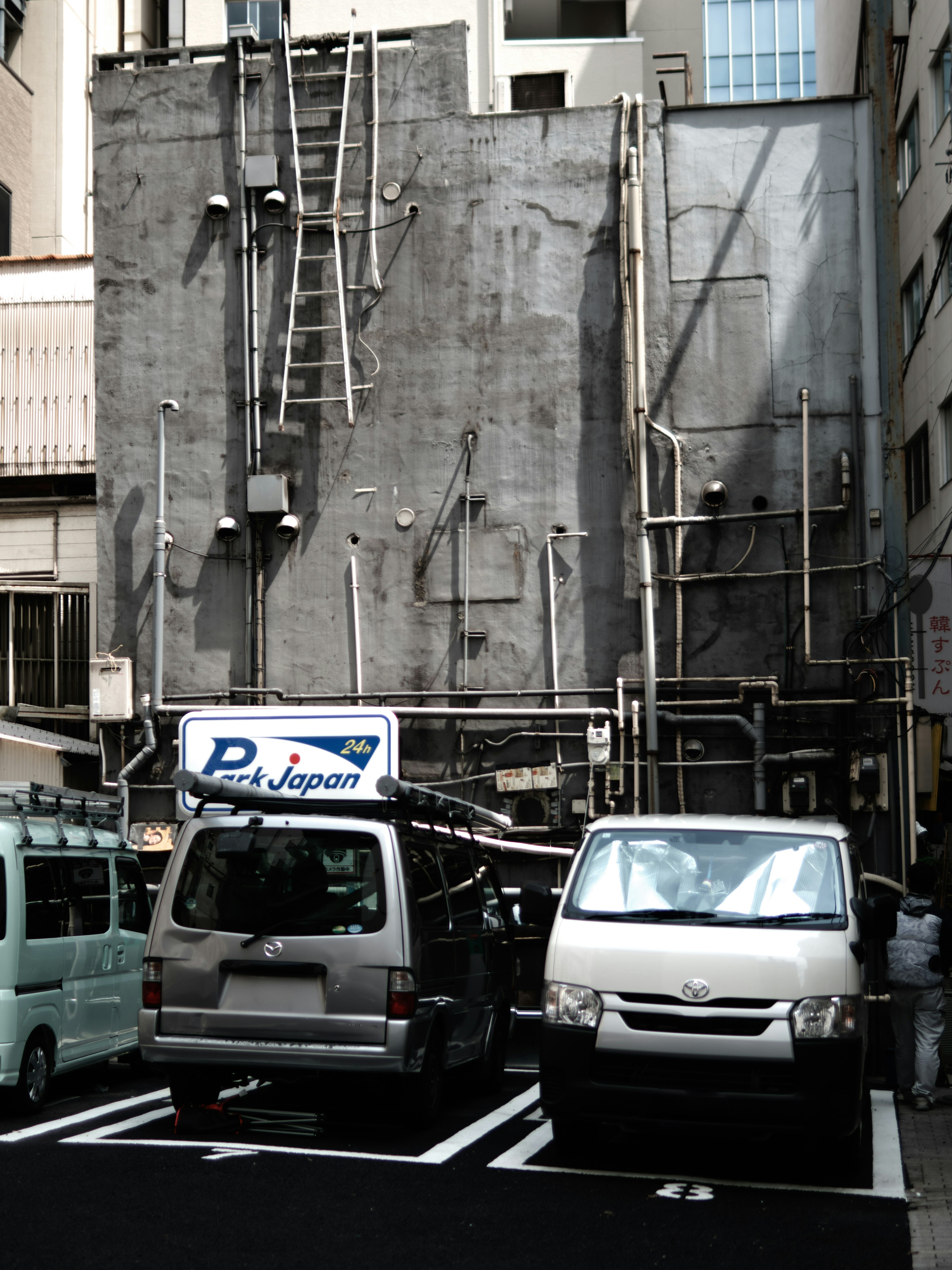 Two parked vehicles in front of a gray wall with visible pipes and a ladder