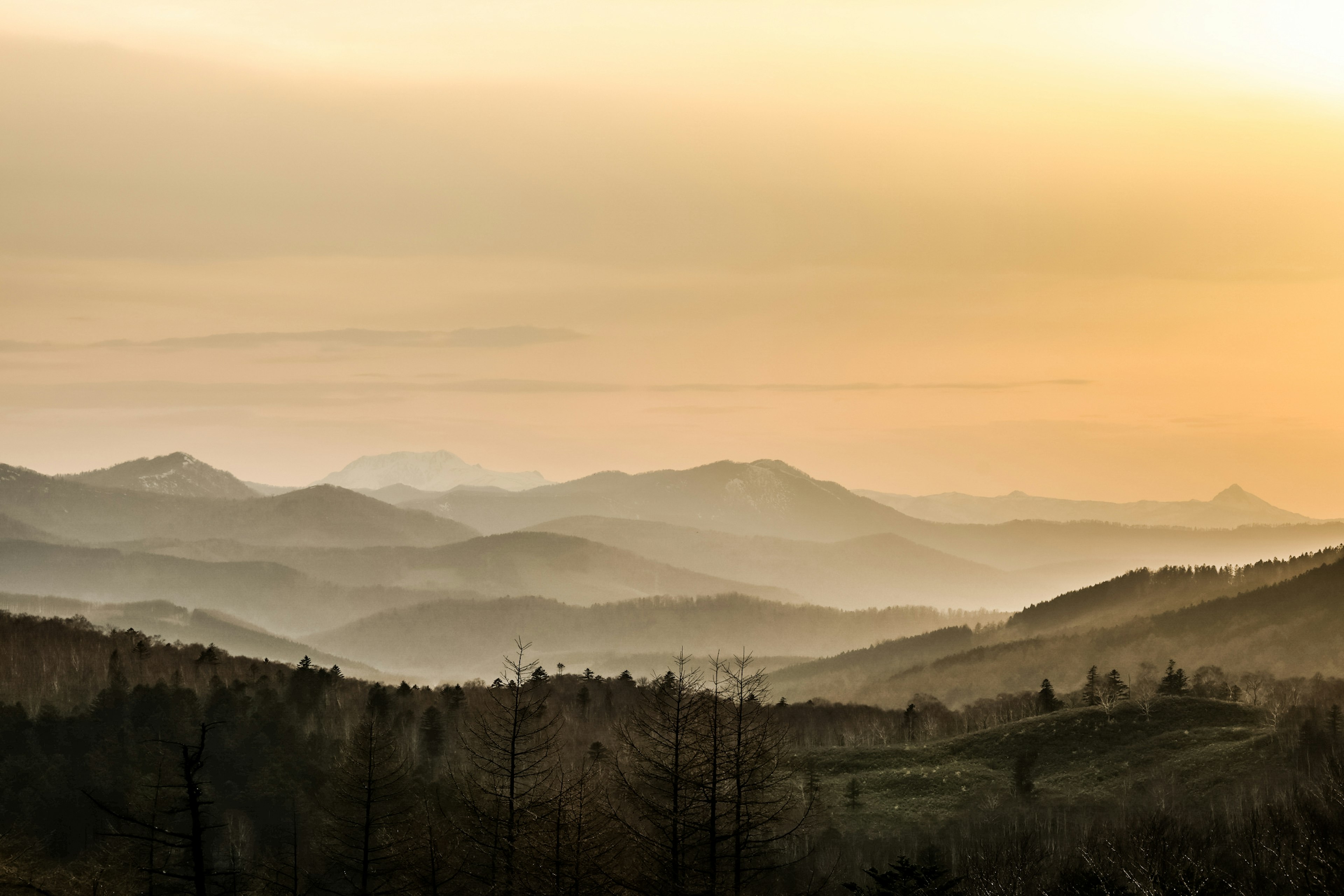 夕暮れの山々が広がる風景　柔らかなオレンジ色の空と霧のかかった丘陵