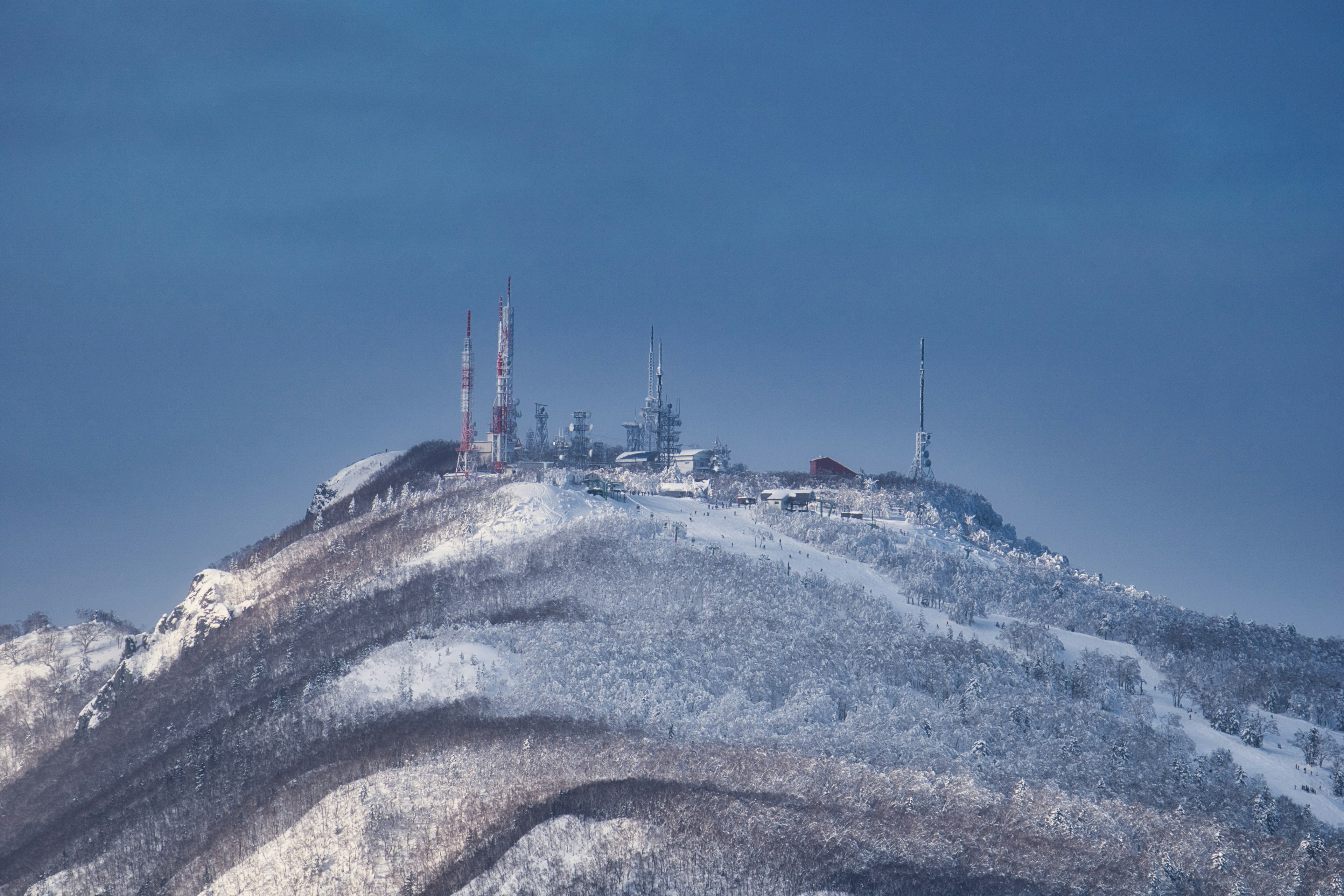 雪に覆われた山頂にある通信塔群と寒冷な空の風景