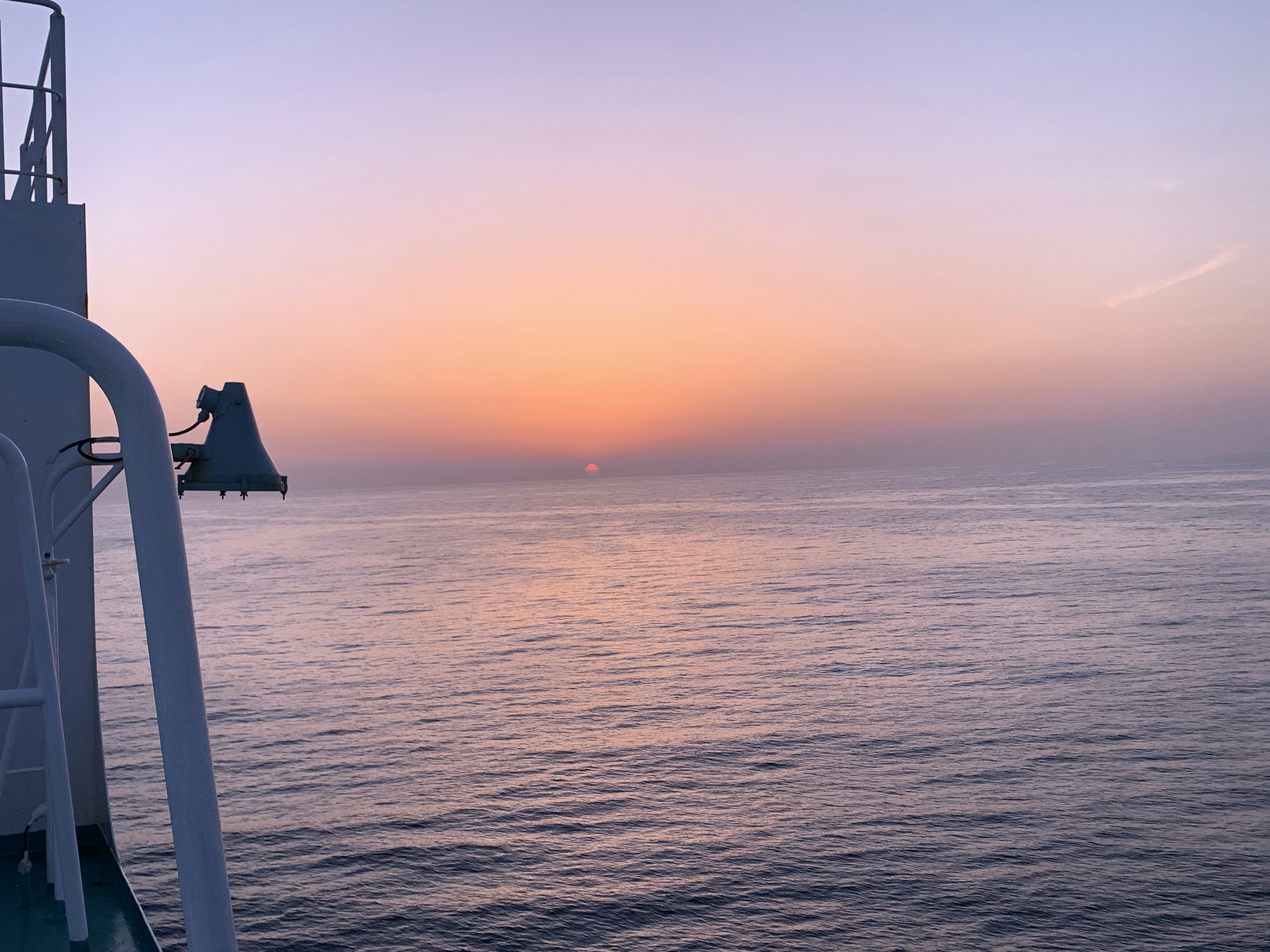 Ruhiges Meer mit Sonnenuntergangshimmel und einem Teil eines Schiffs auf der linken Seite