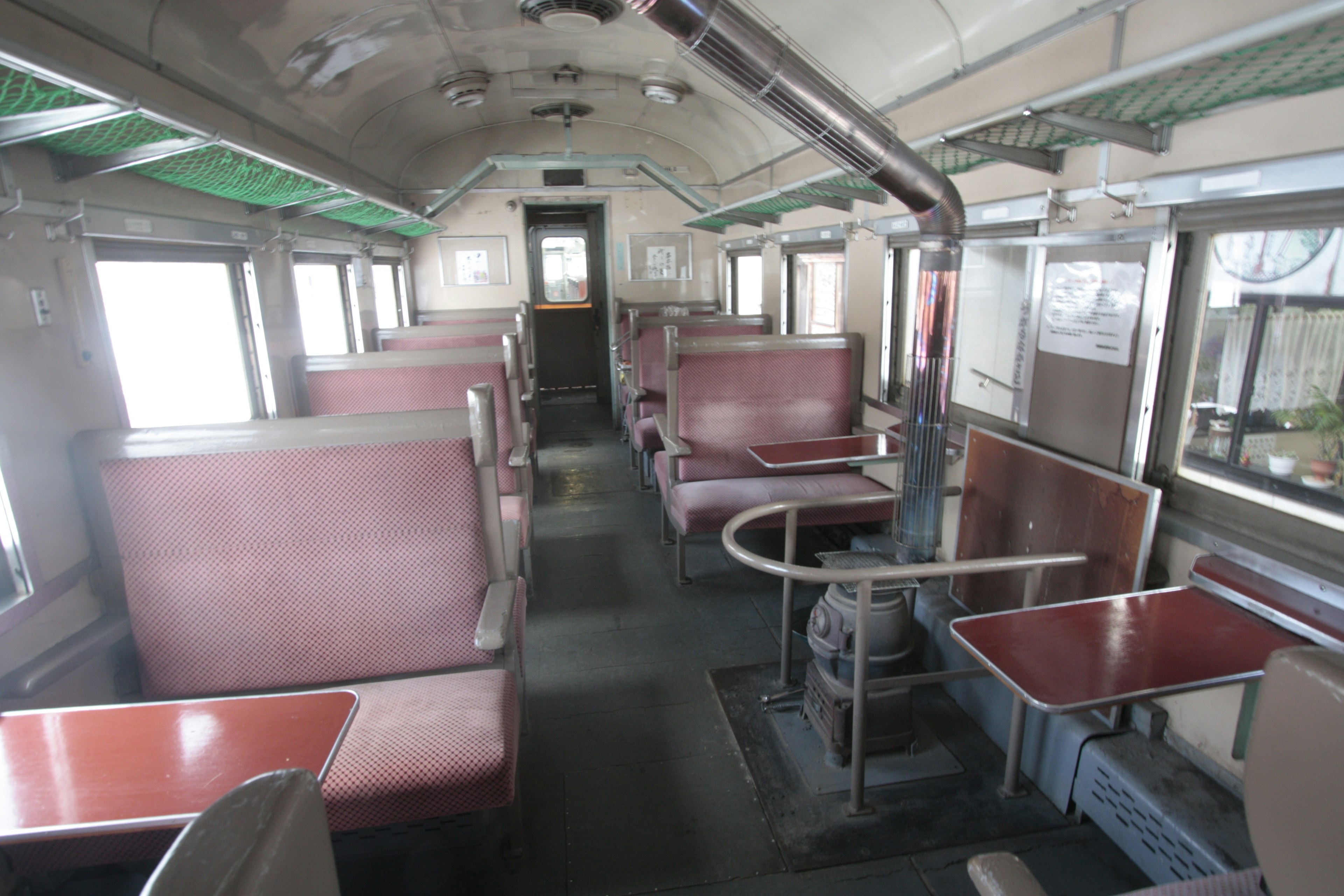 Interior de un viejo vagón de tren con asientos rojos y mesas de diseño simple