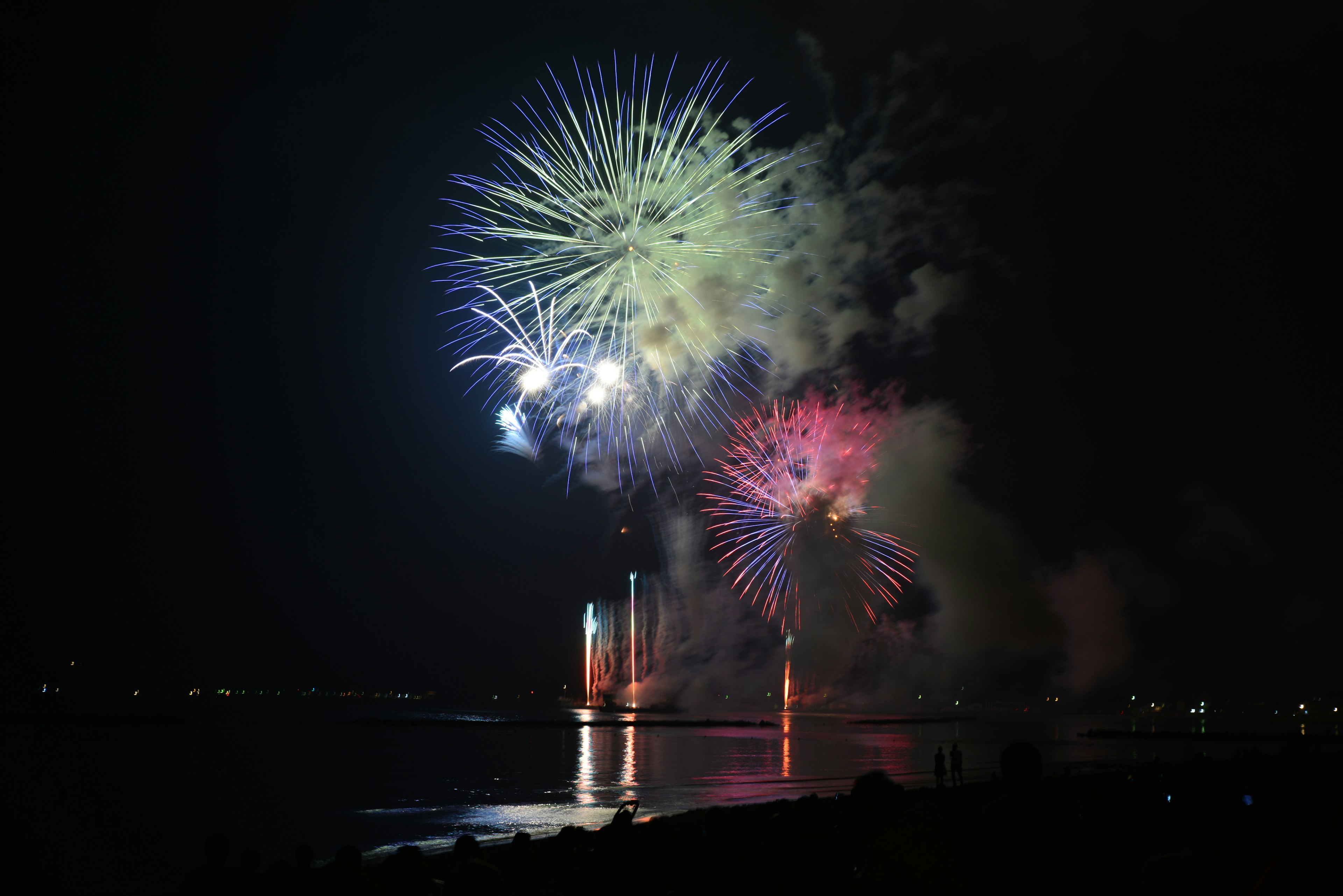 Fuochi d'artificio colorati che esplodono nel cielo notturno riflessi sull'acqua