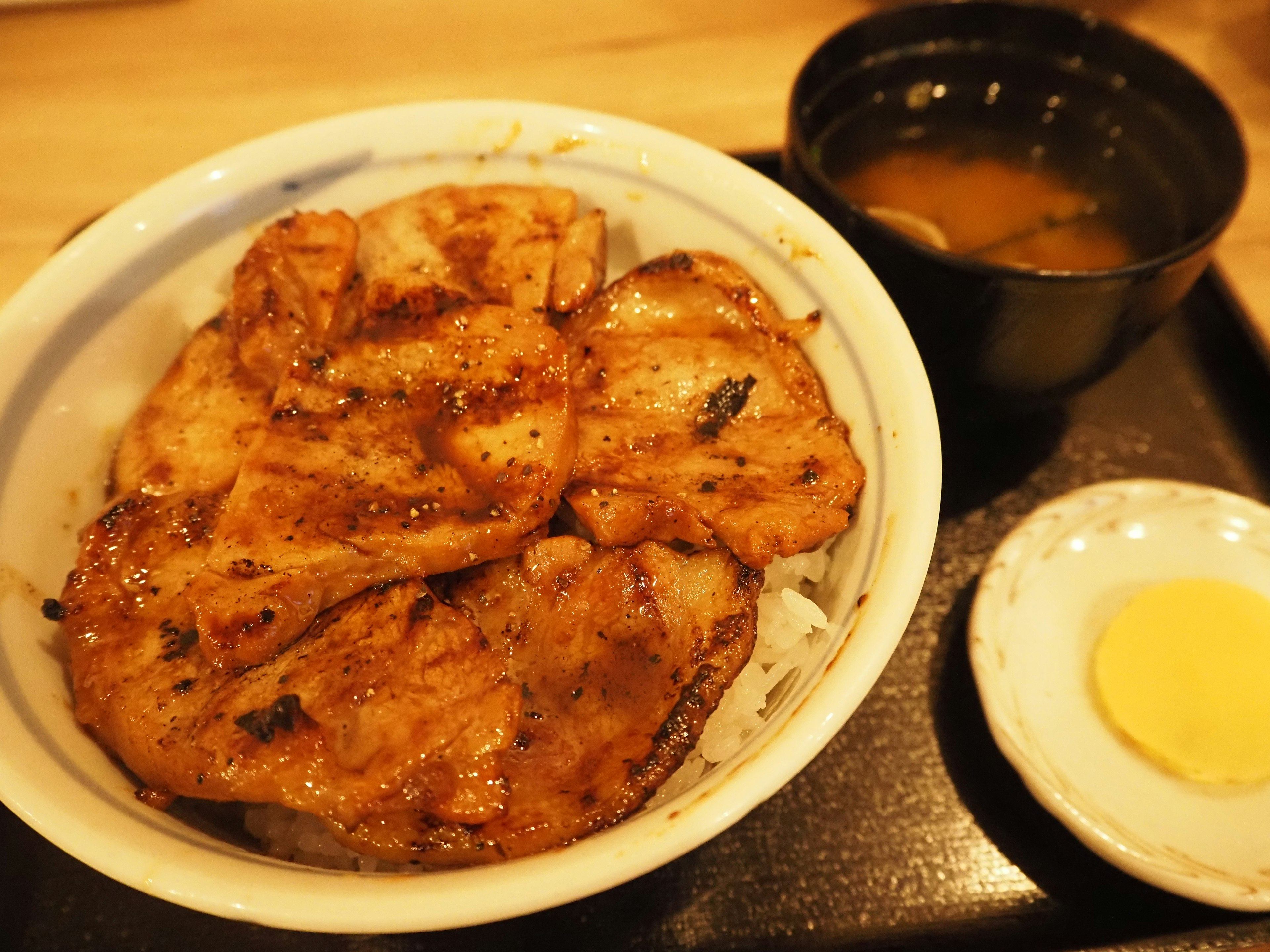 A bowl of rice topped with grilled pork and a side of miso soup