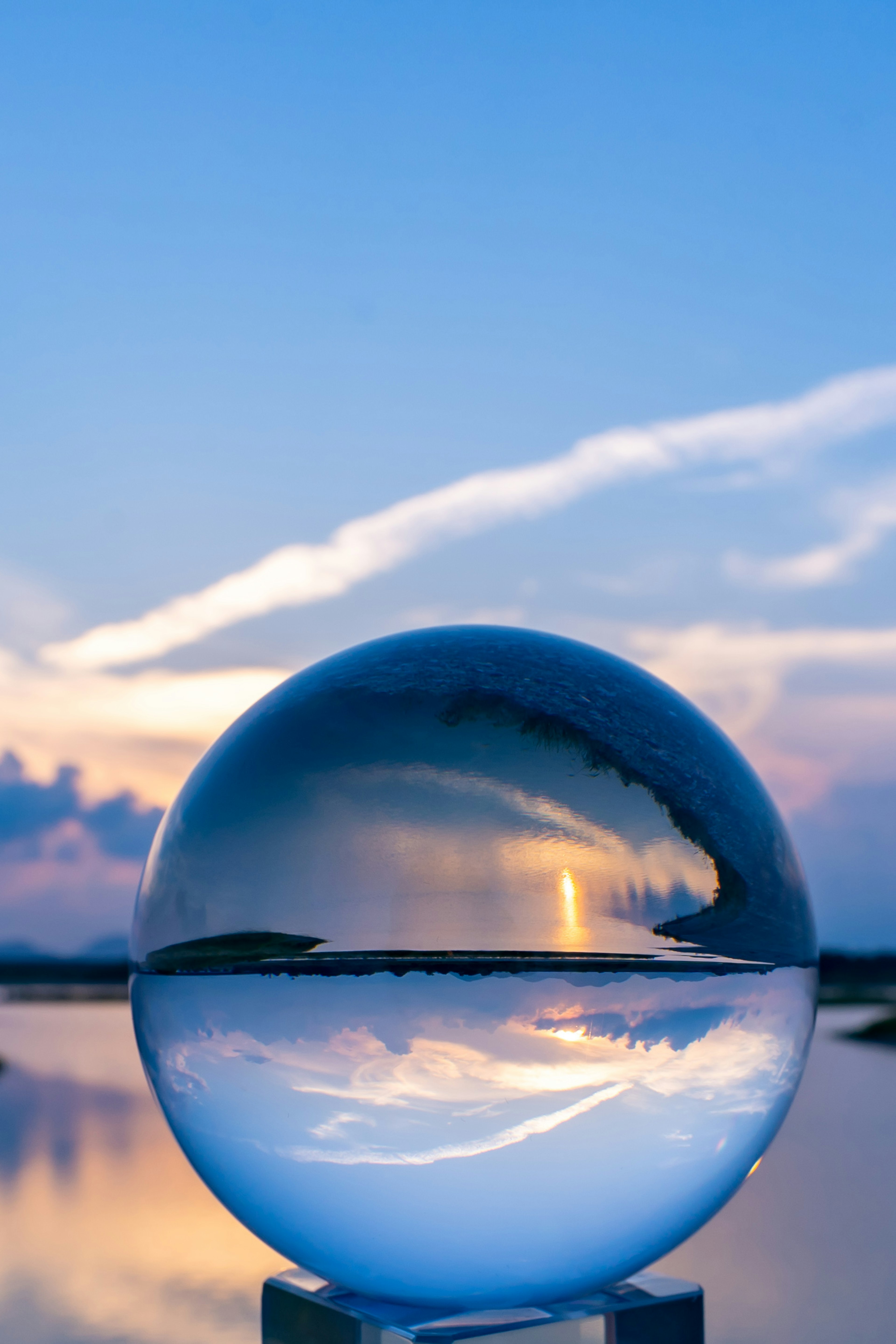 Eine klare Glaskugel, die den blauen Himmel und die Wolken über Wasser reflektiert