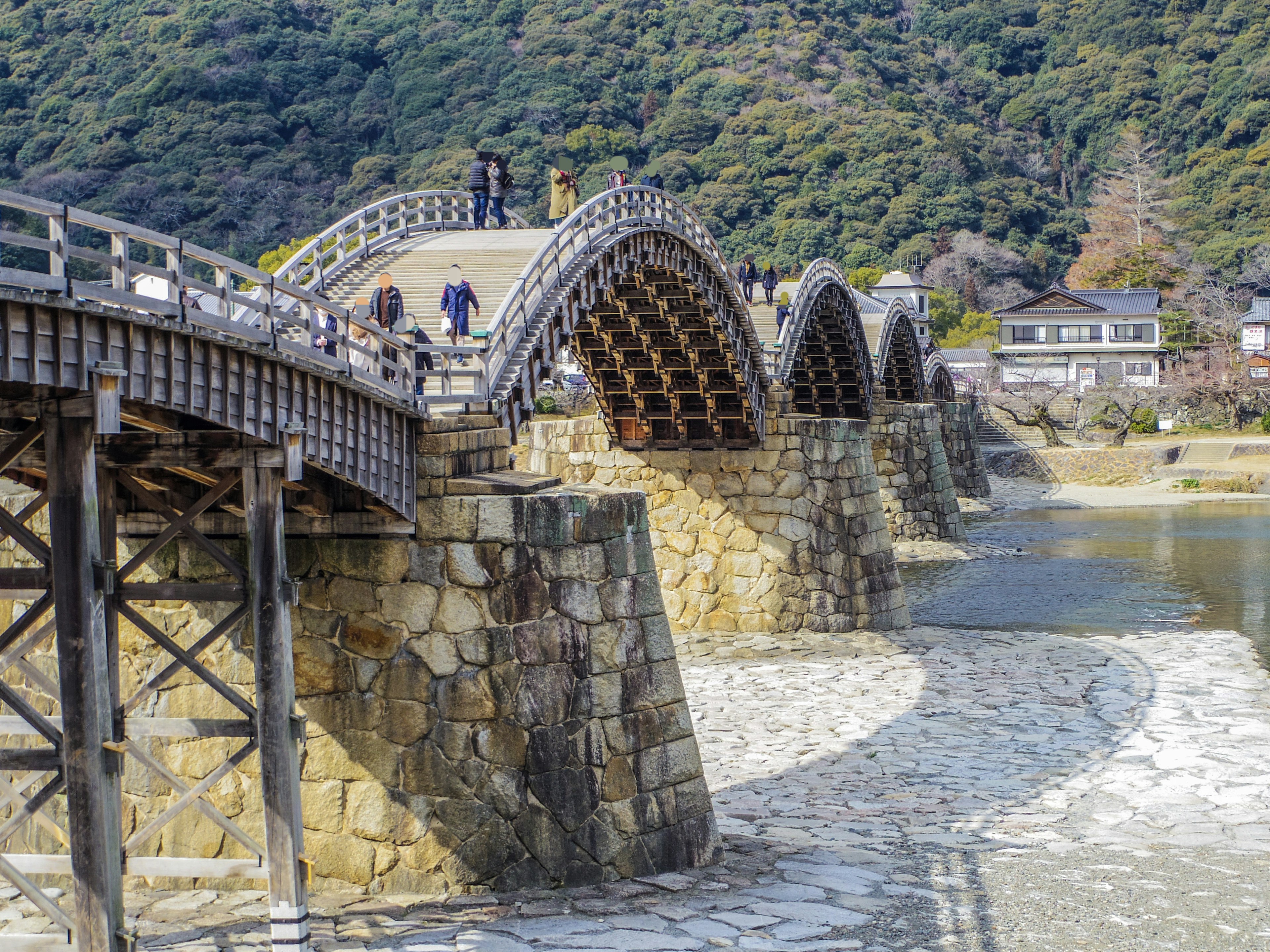 สะพานโค้งไม้สวยงามอยู่บนฐานหินล้อมรอบด้วยภูเขาที่เขียวขจี