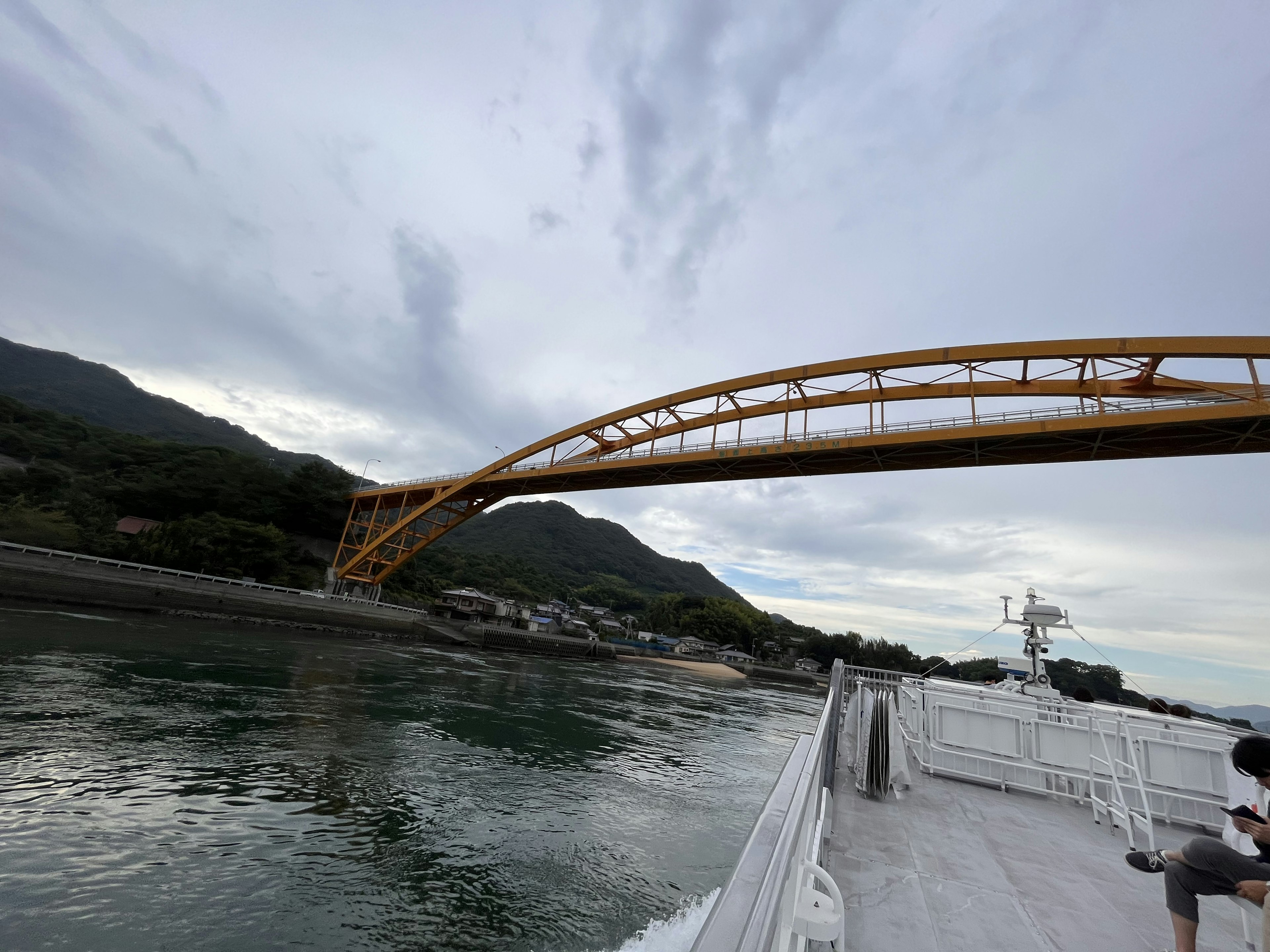 Un pont en arc jaune s'étendant au-dessus de l'eau avec des montagnes en arrière-plan