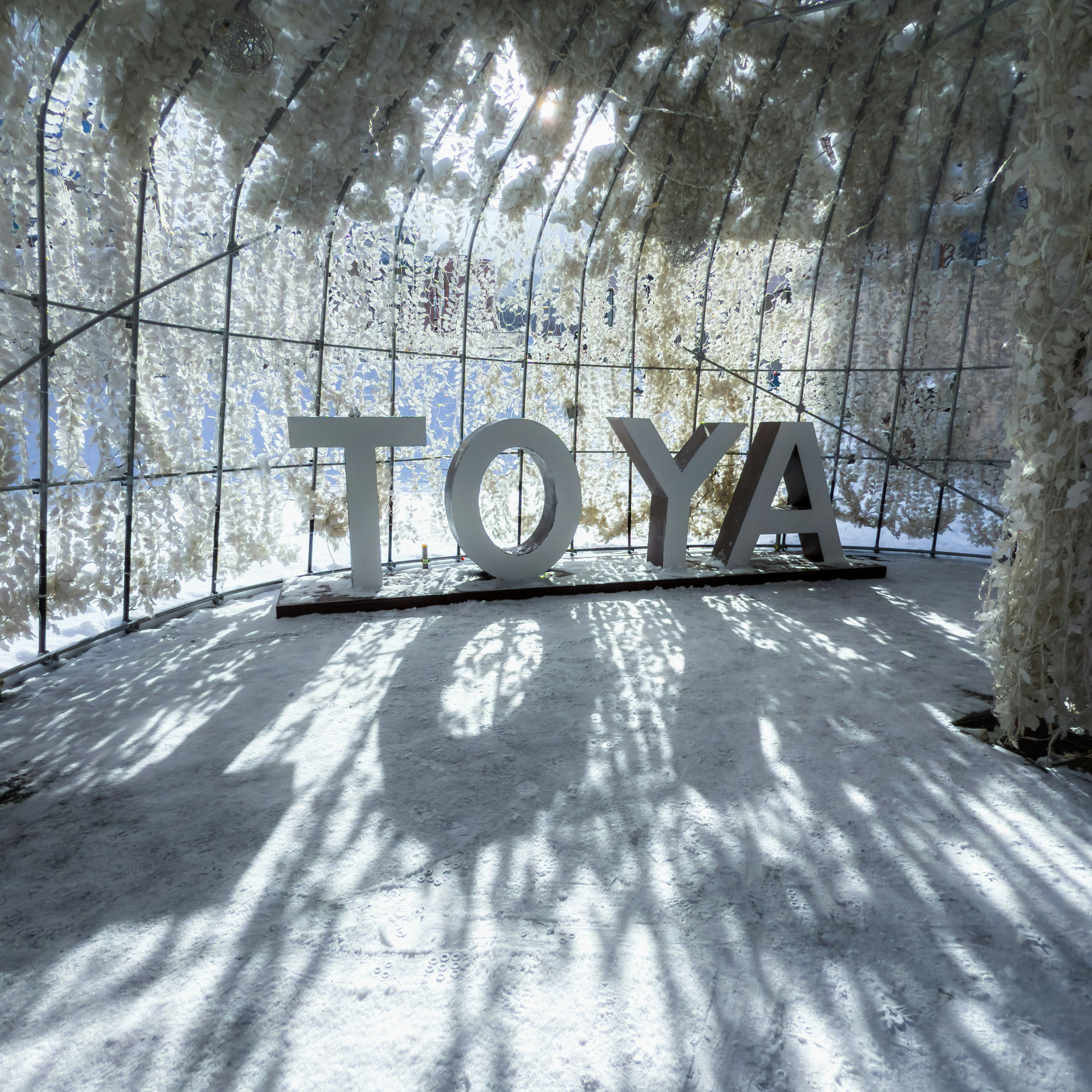 Ein verschneiter Raum mit großen Buchstaben, die 'TOYA' in einer künstlerischen Installation bilden