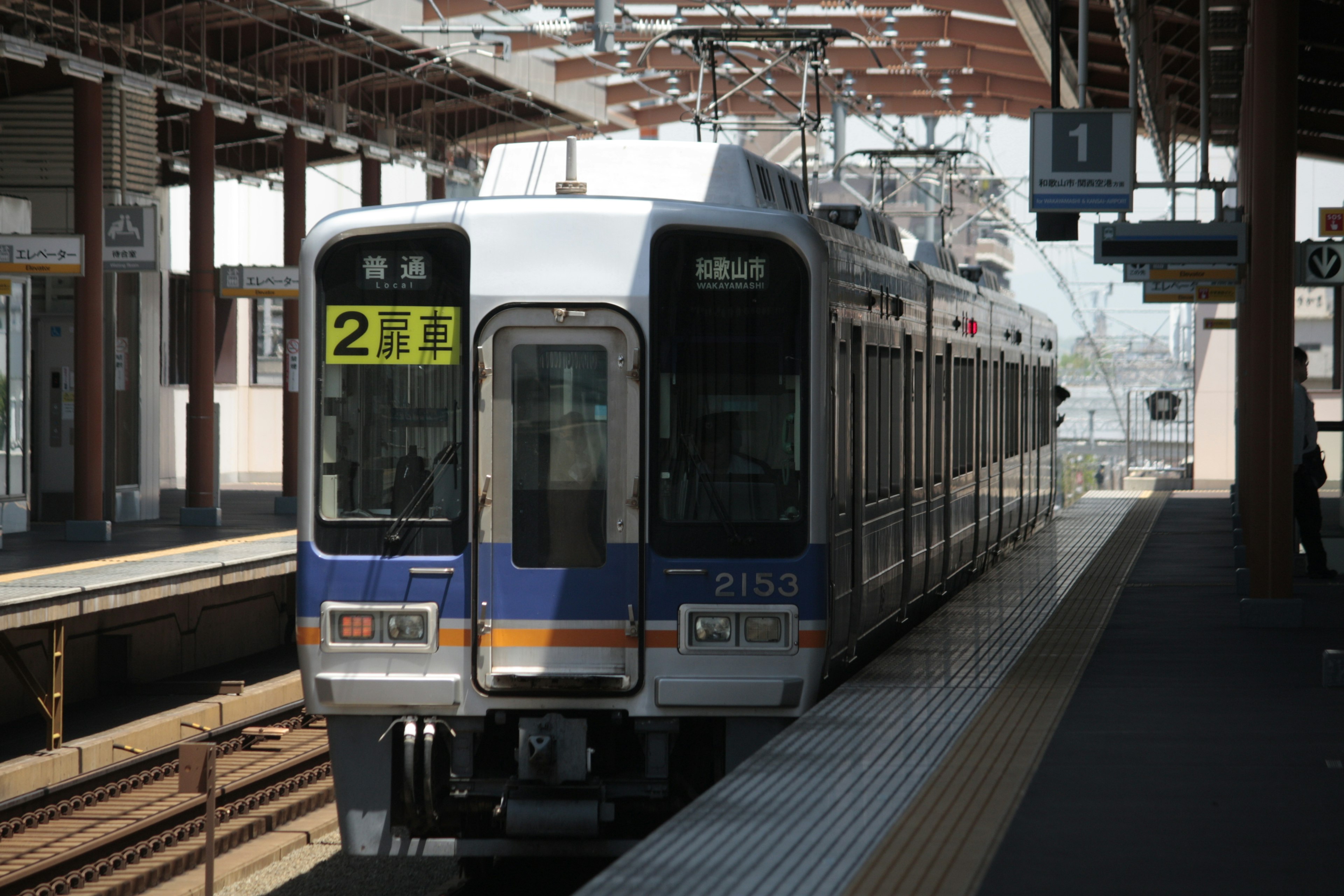 รถไฟที่หยุดอยู่ที่ชานชาลาสถานีพร้อมป้ายและโครงสร้างที่มองเห็นได้