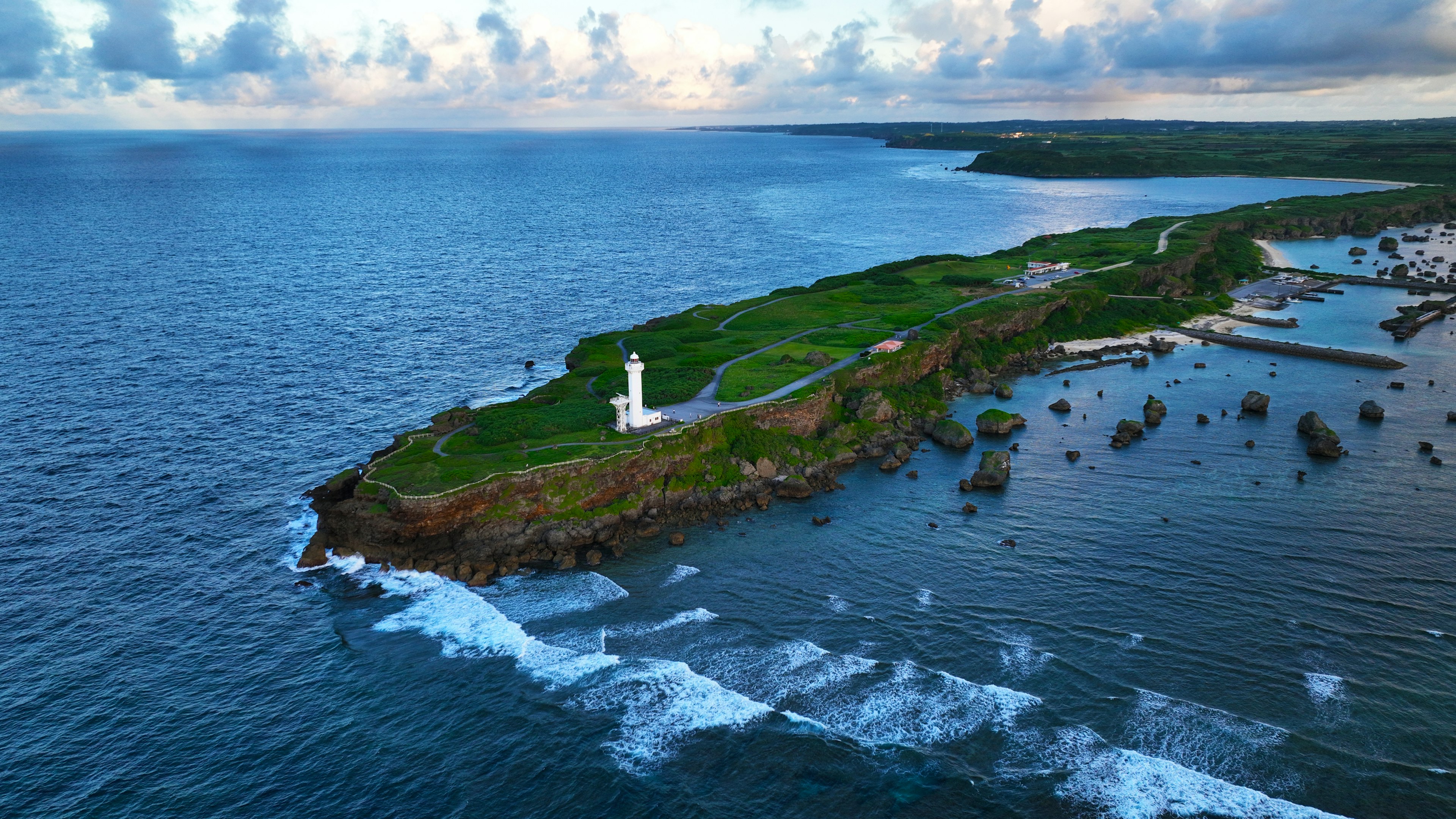 A white lighthouse on a green cliff overlooking the blue ocean