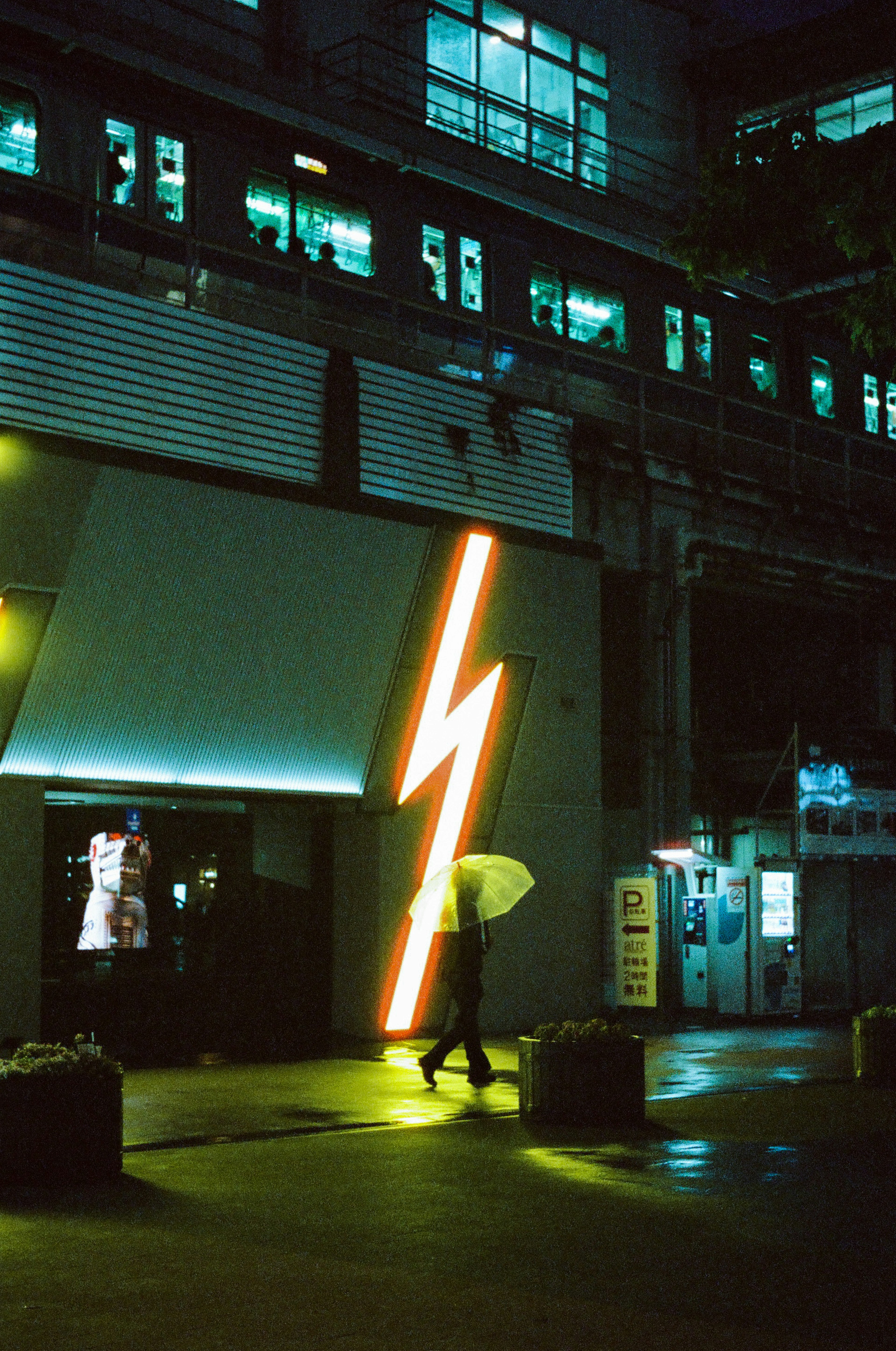 Une personne avec un parapluie marchant sous un panneau néon en forme d'éclair la nuit