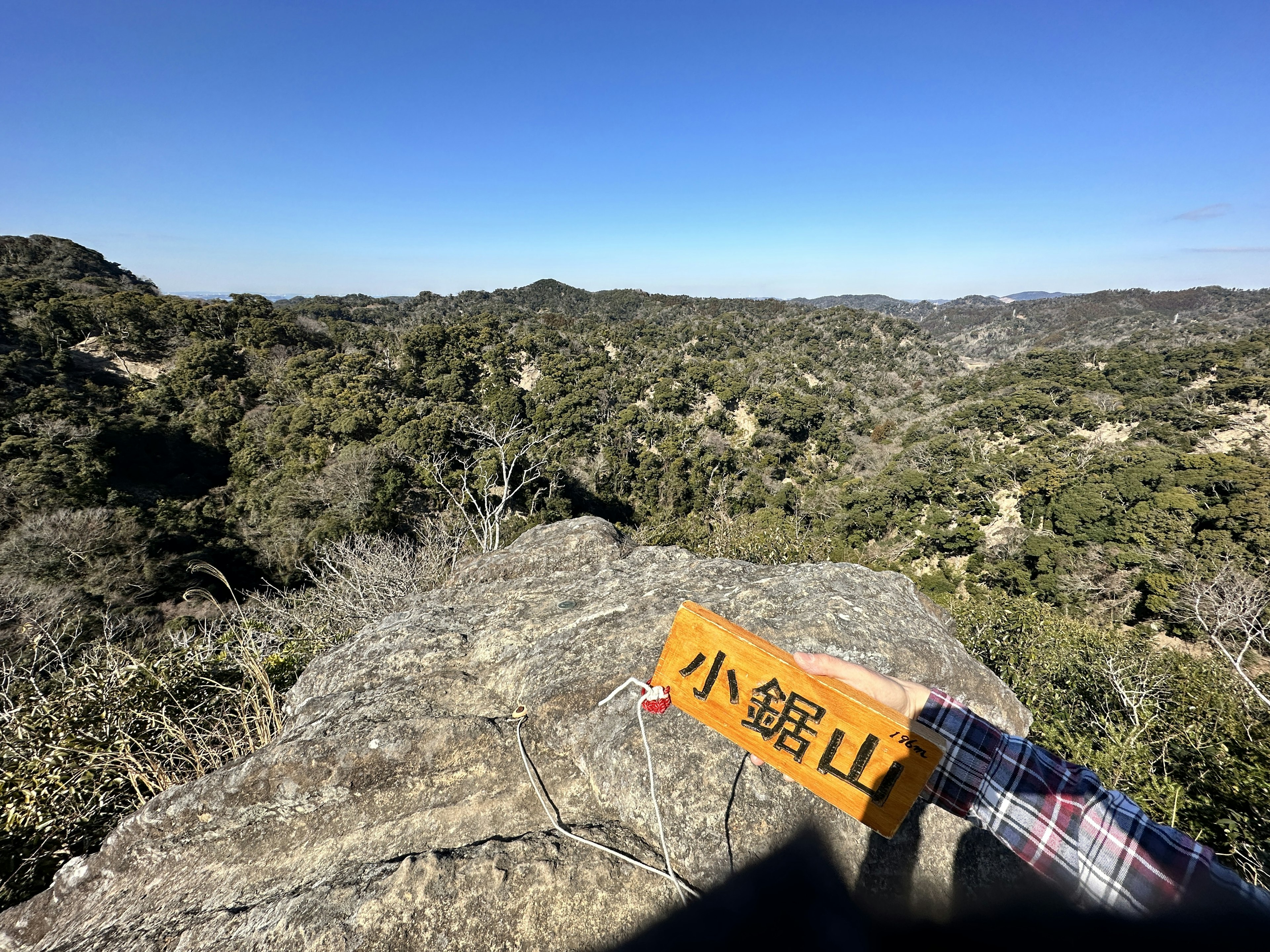 View from a rocky outcrop with a sign for Kobayashi Mountain surrounded by lush green hills and clear blue sky