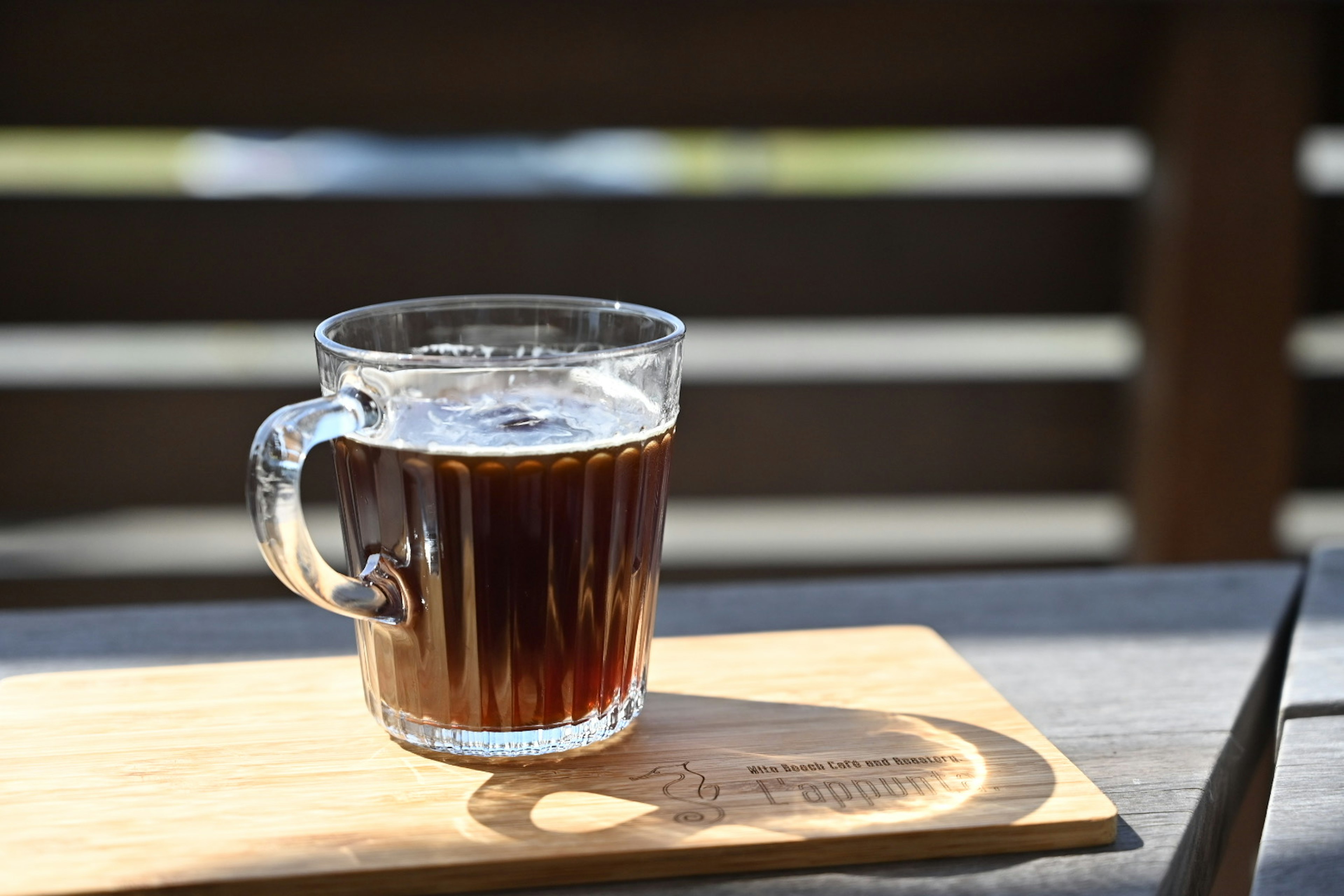 Cangkir kaca transparan berisi kopi diletakkan di atas nampan kayu