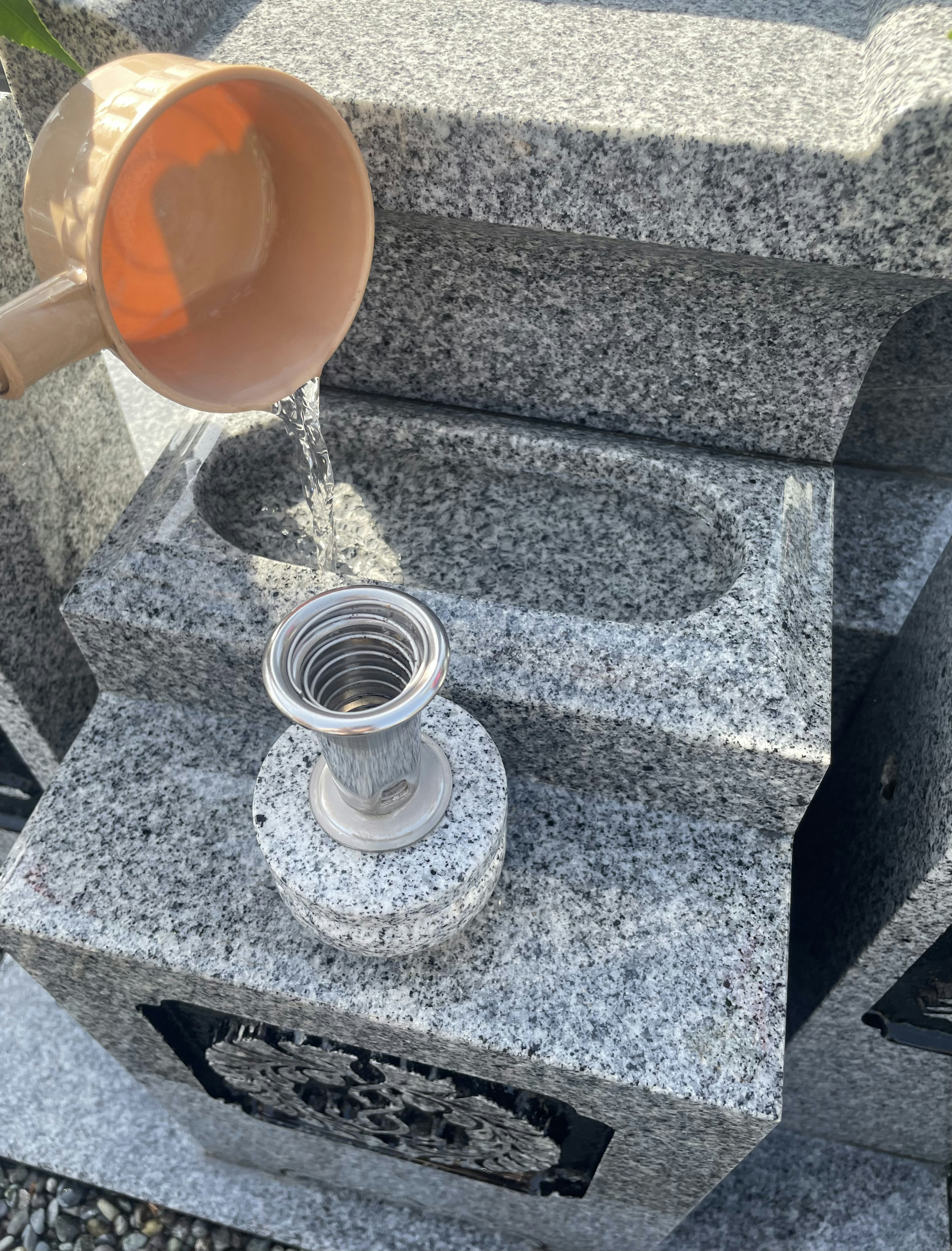 A ceramic watering can pouring water over a gray stone memorial