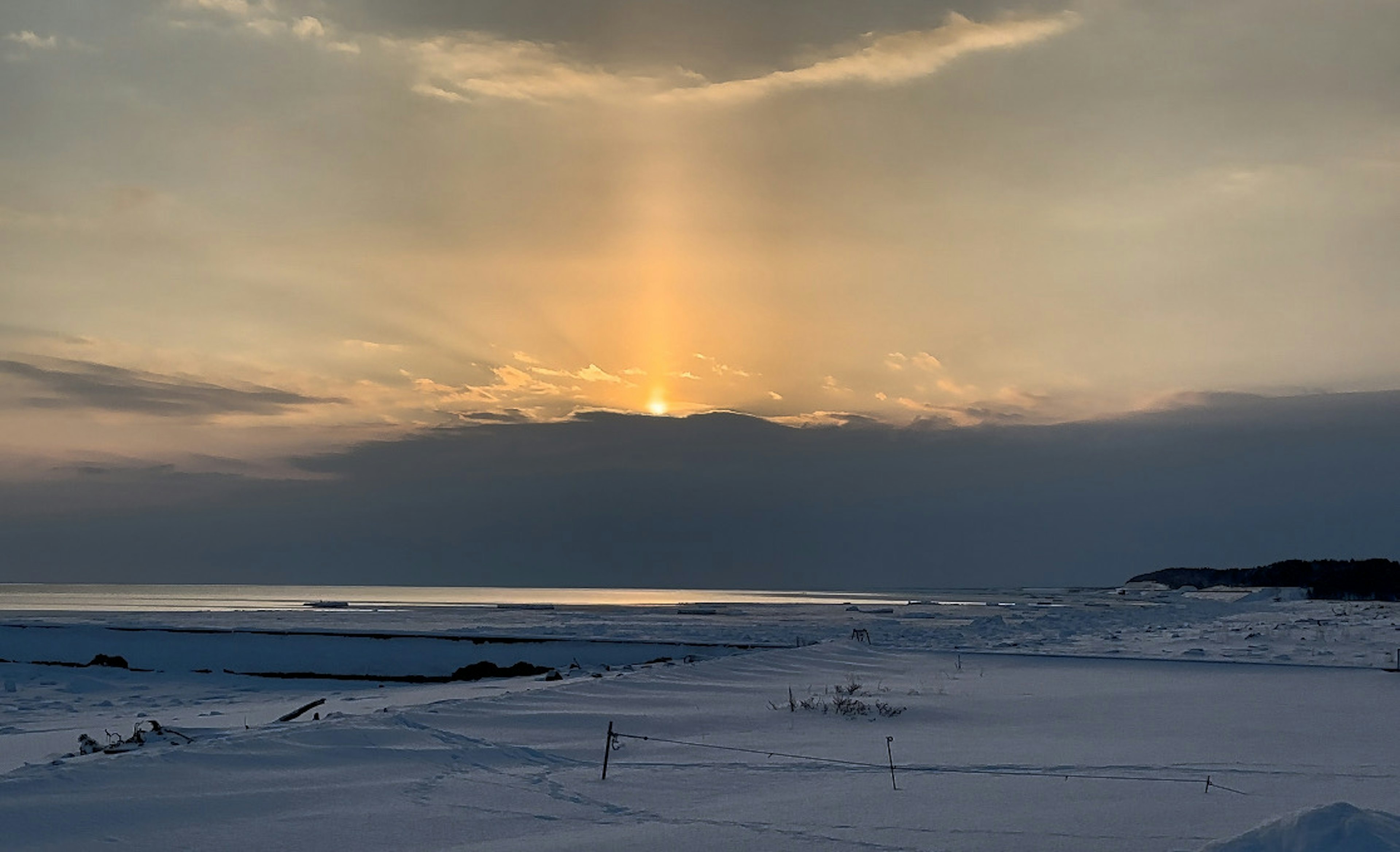 Tramonto che illumina un paesaggio innevato con raggi di luce che attraversano le nuvole