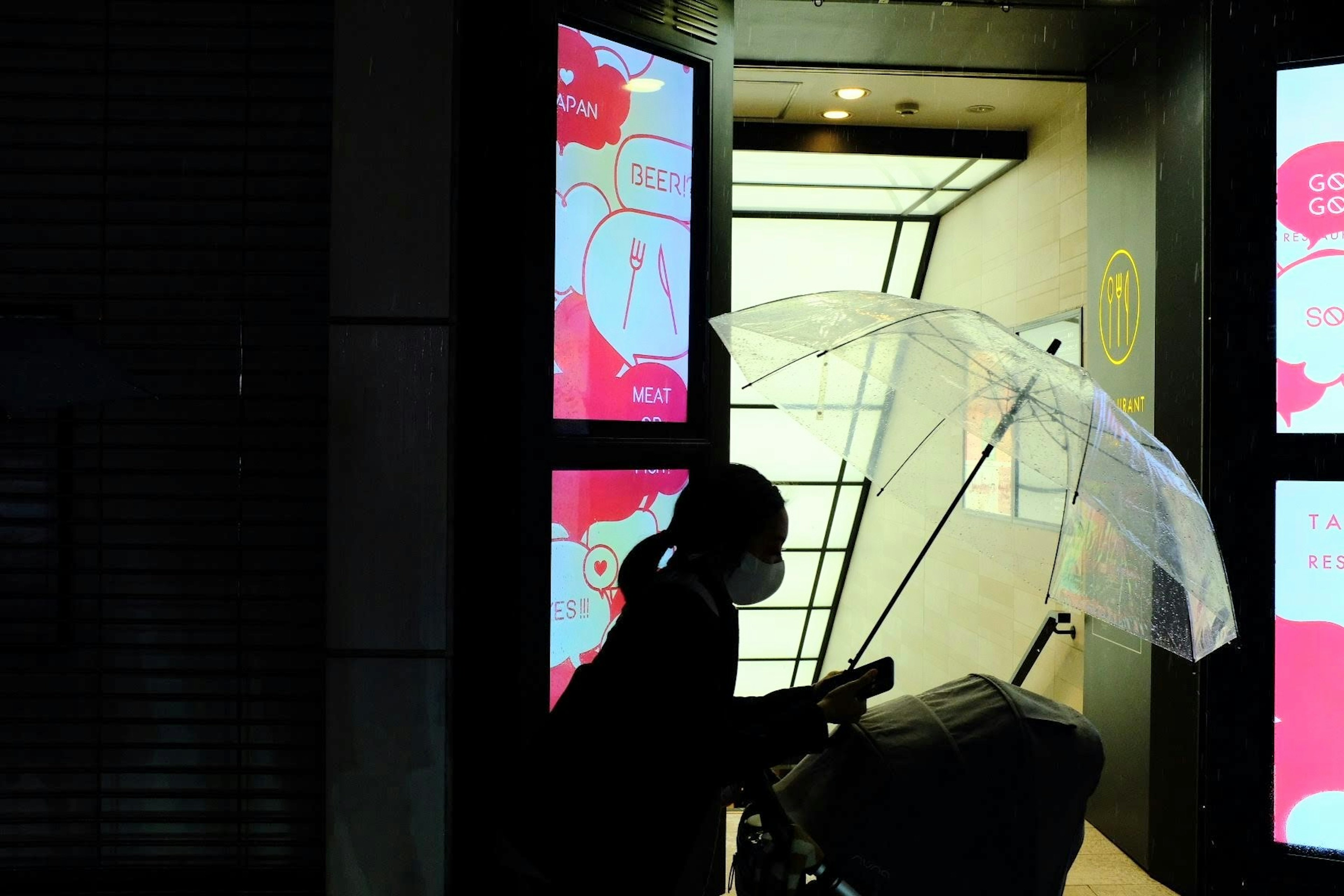 Silhouette of a person holding an umbrella standing in front of an elevator illuminated by bright signs at night