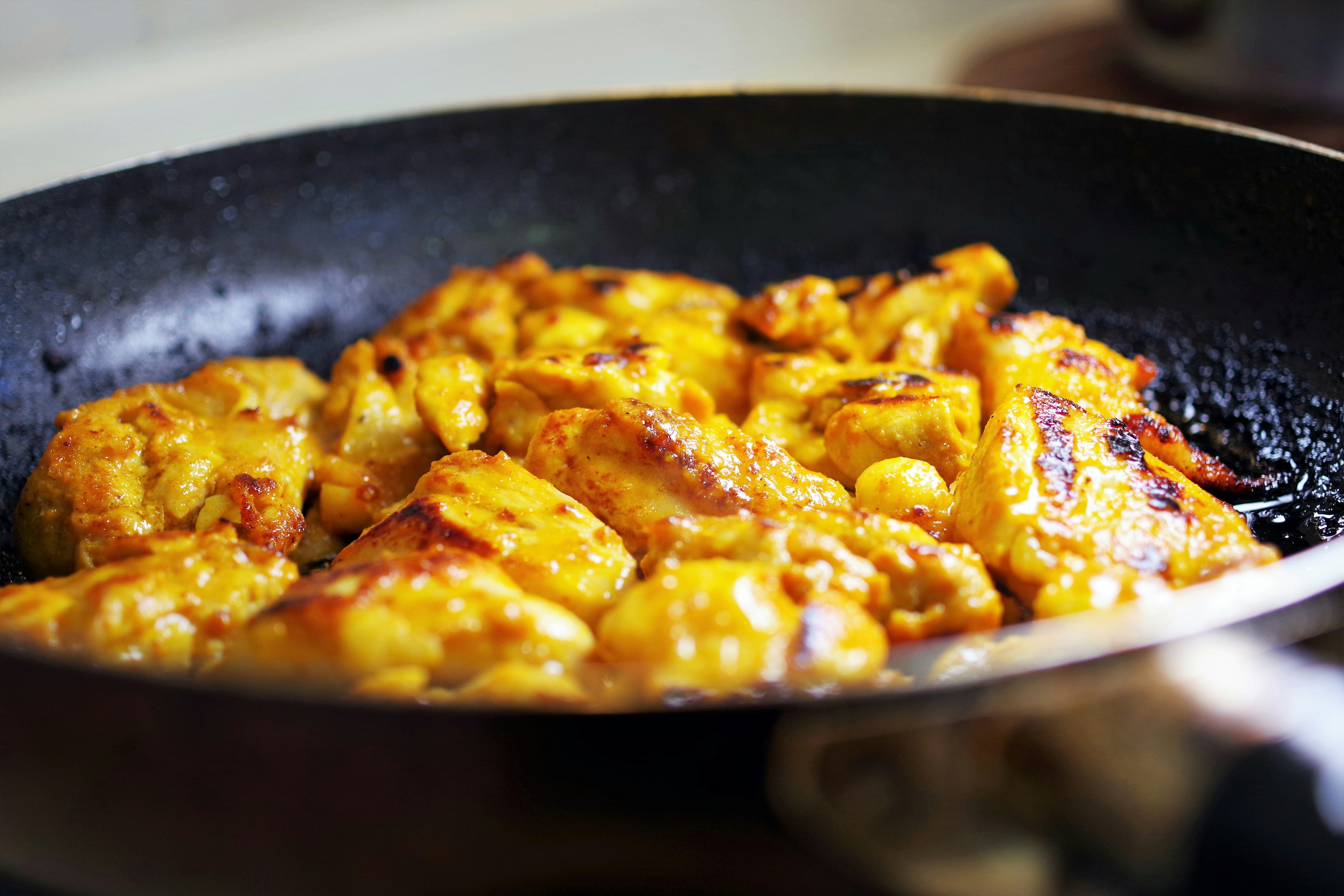 Trozos de pollo dorados cocinándose en una sartén