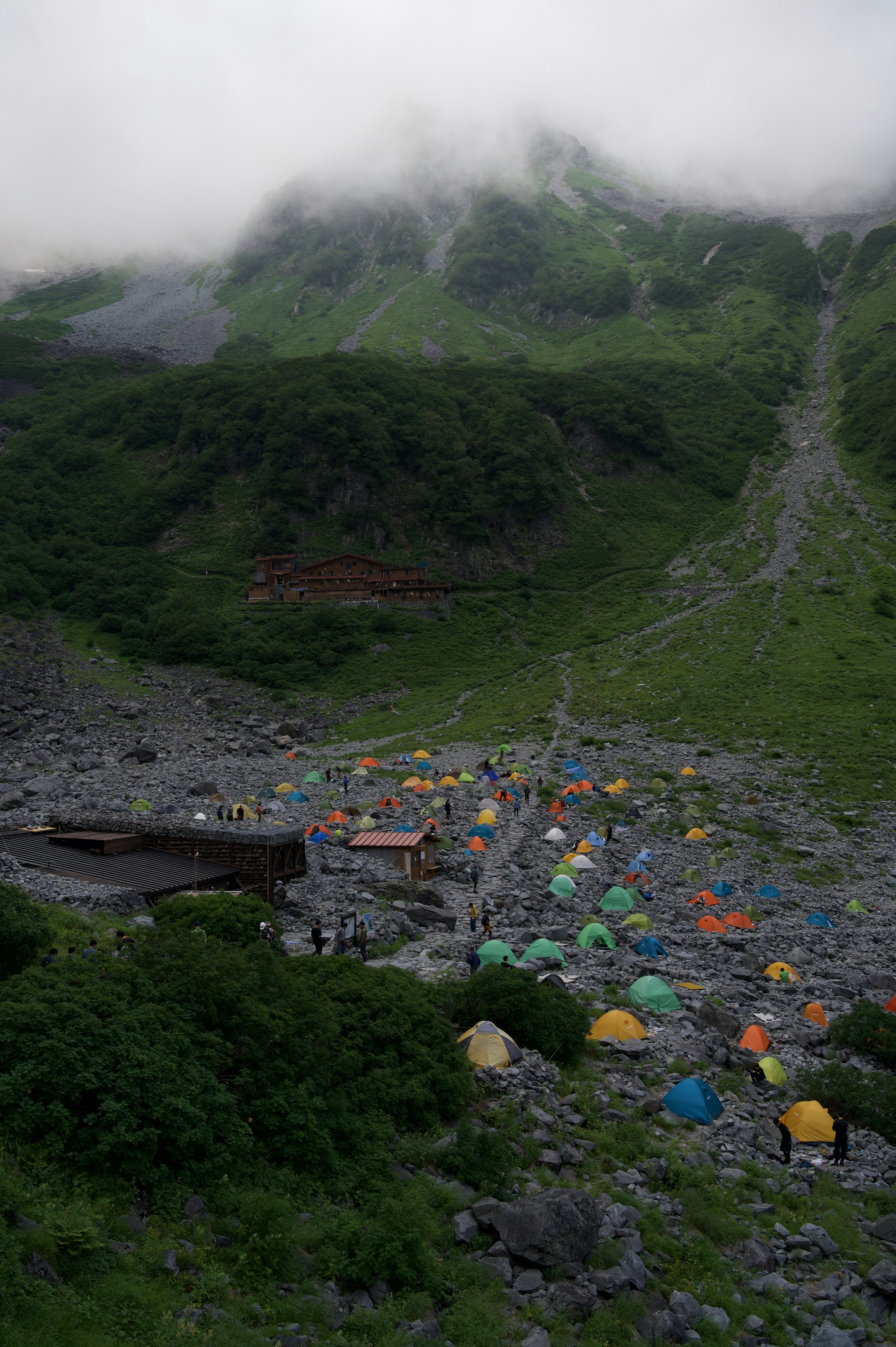 Colorful tent campsite surrounded by mountains and green slopes under fog