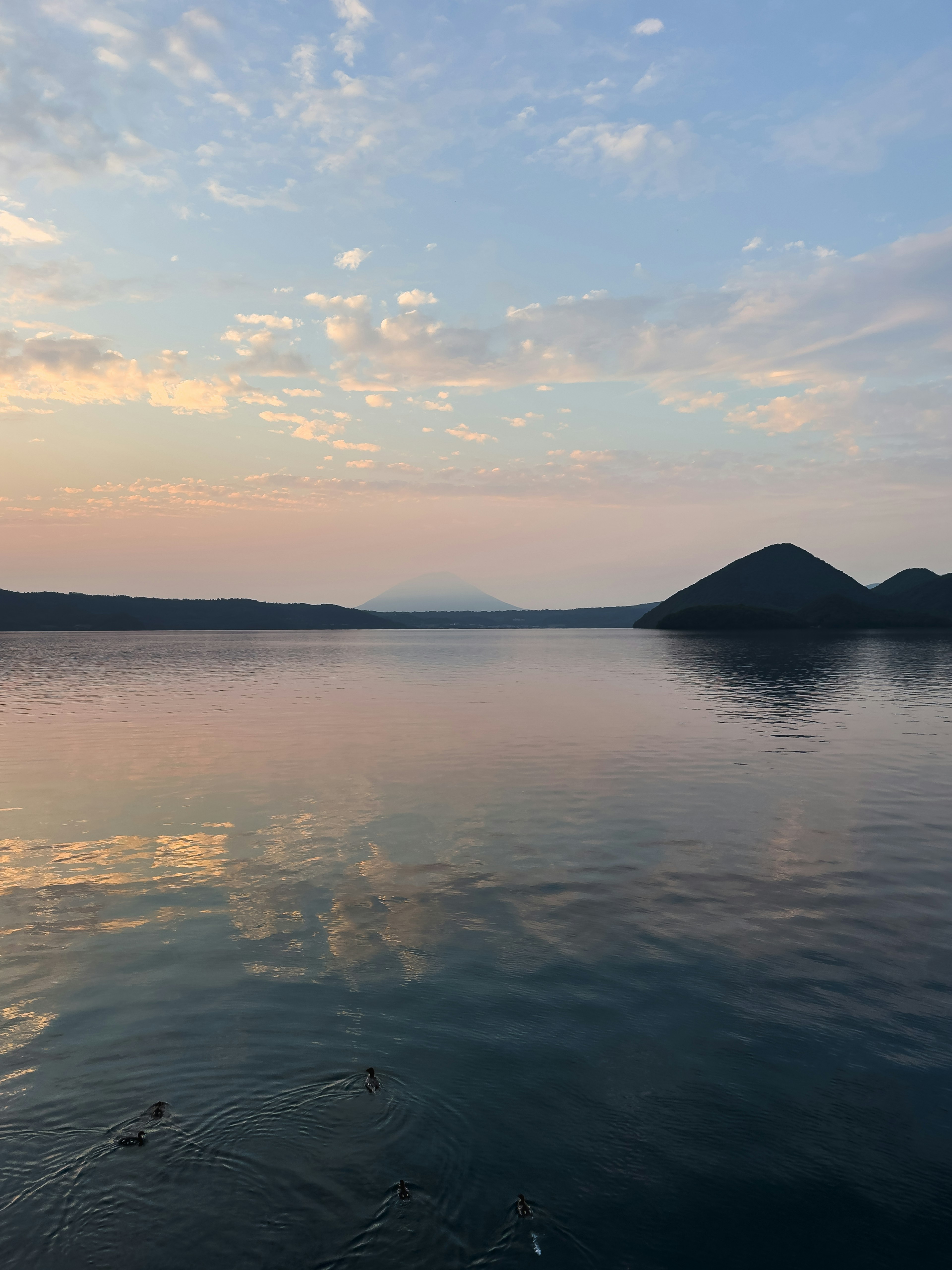 Ruhiger See, der einen Sonnenuntergangshimmel und Silhouetten von Bergen widerspiegelt