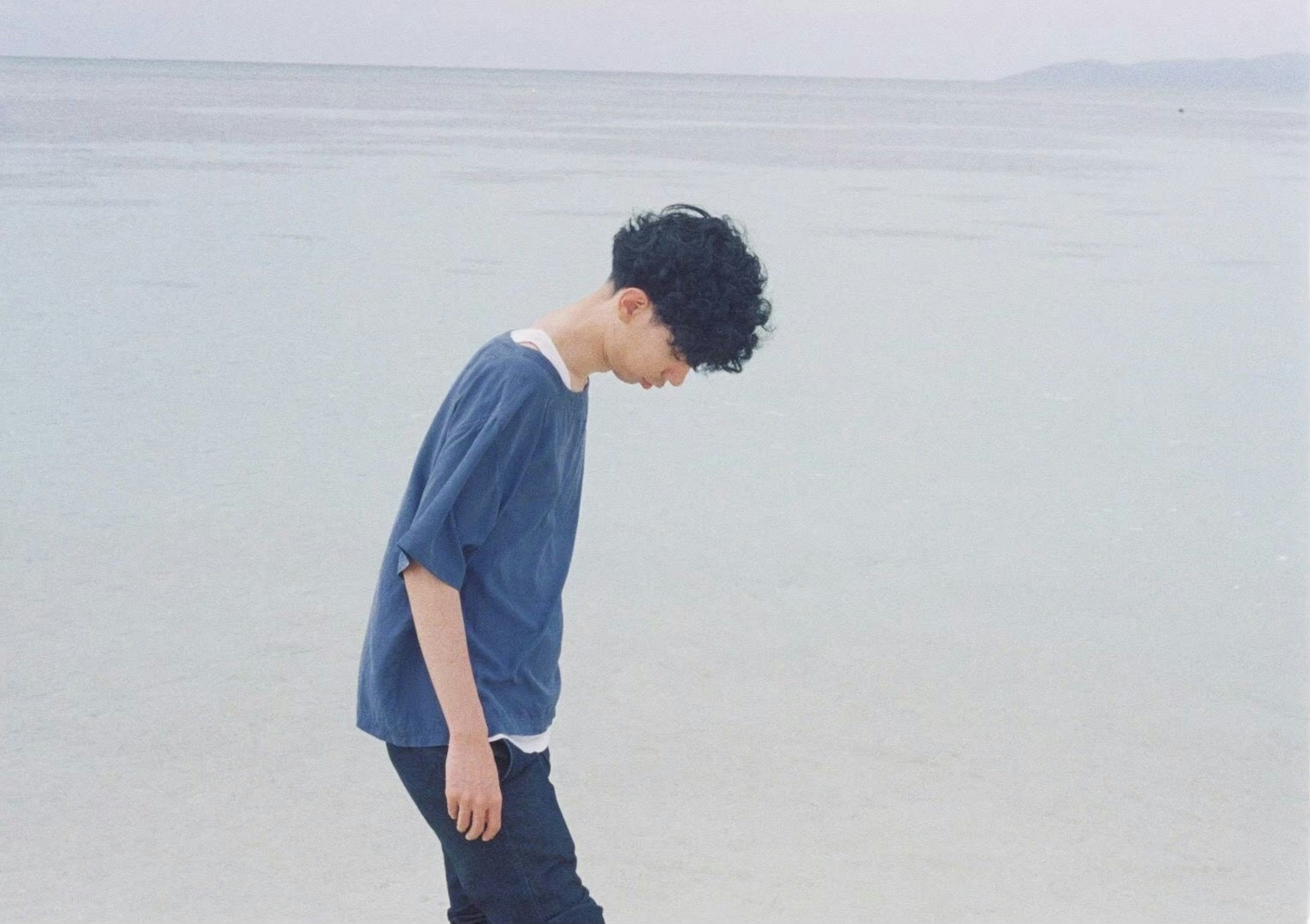 Un uomo in camicia blu che guarda verso il basso sulla spiaggia