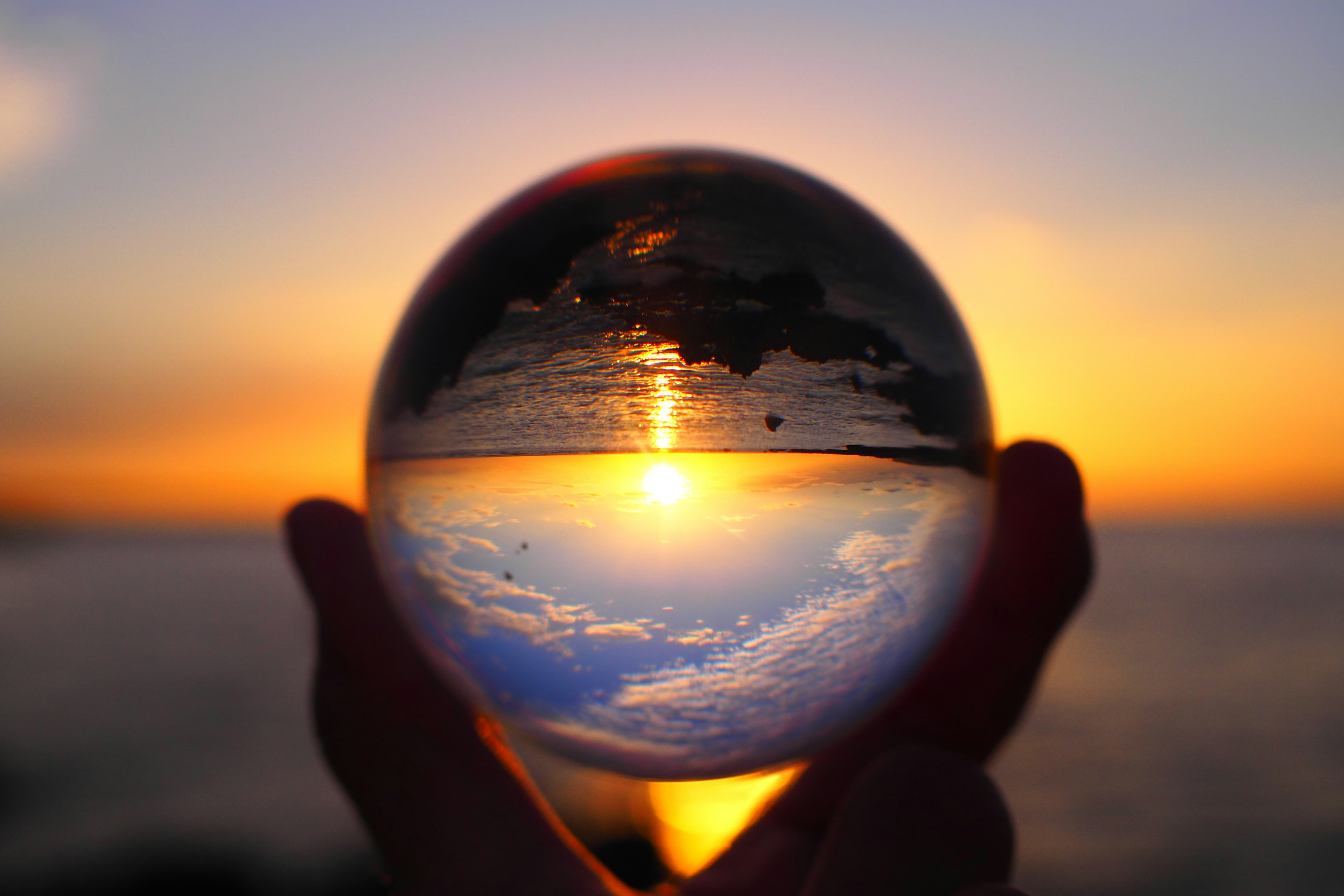 Silhouette che tiene una sfera di cristallo che riflette un tramonto sull'oceano